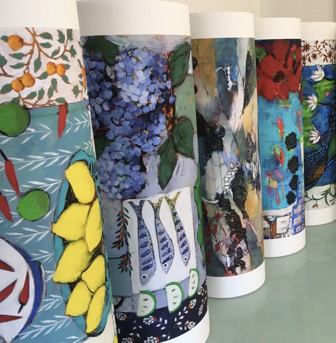 Colorful rolls of printed fabric showing various floral and fruit patterns, including lemons, berries, leaves, and abstract designs.