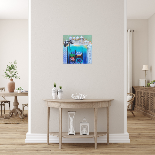 Interior view of a home featuring a small wooden console table against a white wall, decorated with white vases and a white coral centerpiece, with a colorful framed painting above. To the left, there's a dining area with a round wooden table and chairs, and to the right, a sideboard with decor and a framed picture, all with a light-colored hardwood floor.