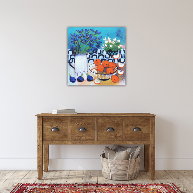 Painting of potted flowers and orange fruit on a table, hung on a plain white wall above a wooden console table with a basket below.