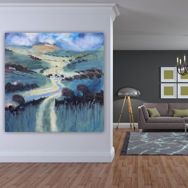 A large landscape painting of a hilly countryside with green fields, trees, a winding road, and a blue sky with clouds hanging over a modern living room.