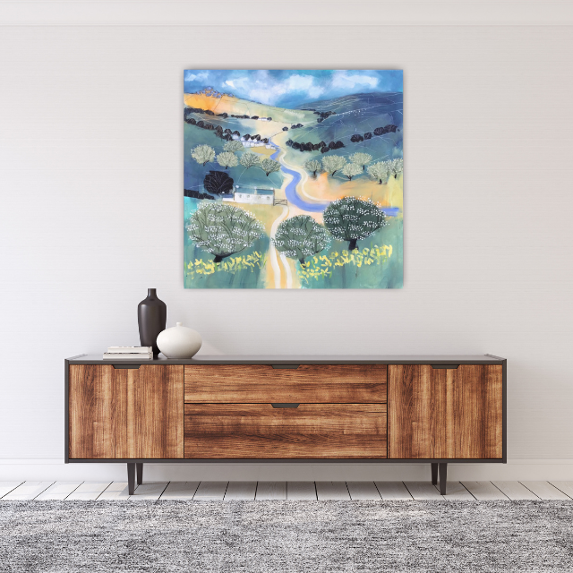 Colorful landscape painting of a countryside with trees, a river, hills, and a cloudy sky, hung above a wooden sideboard with vases.