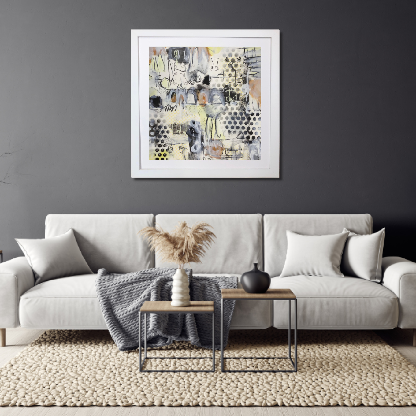 Modern living room with a white sofa, decorative pillows, a gray blanket, a textured rug, and a coffee table with vases, against a gray wall with abstract art.
