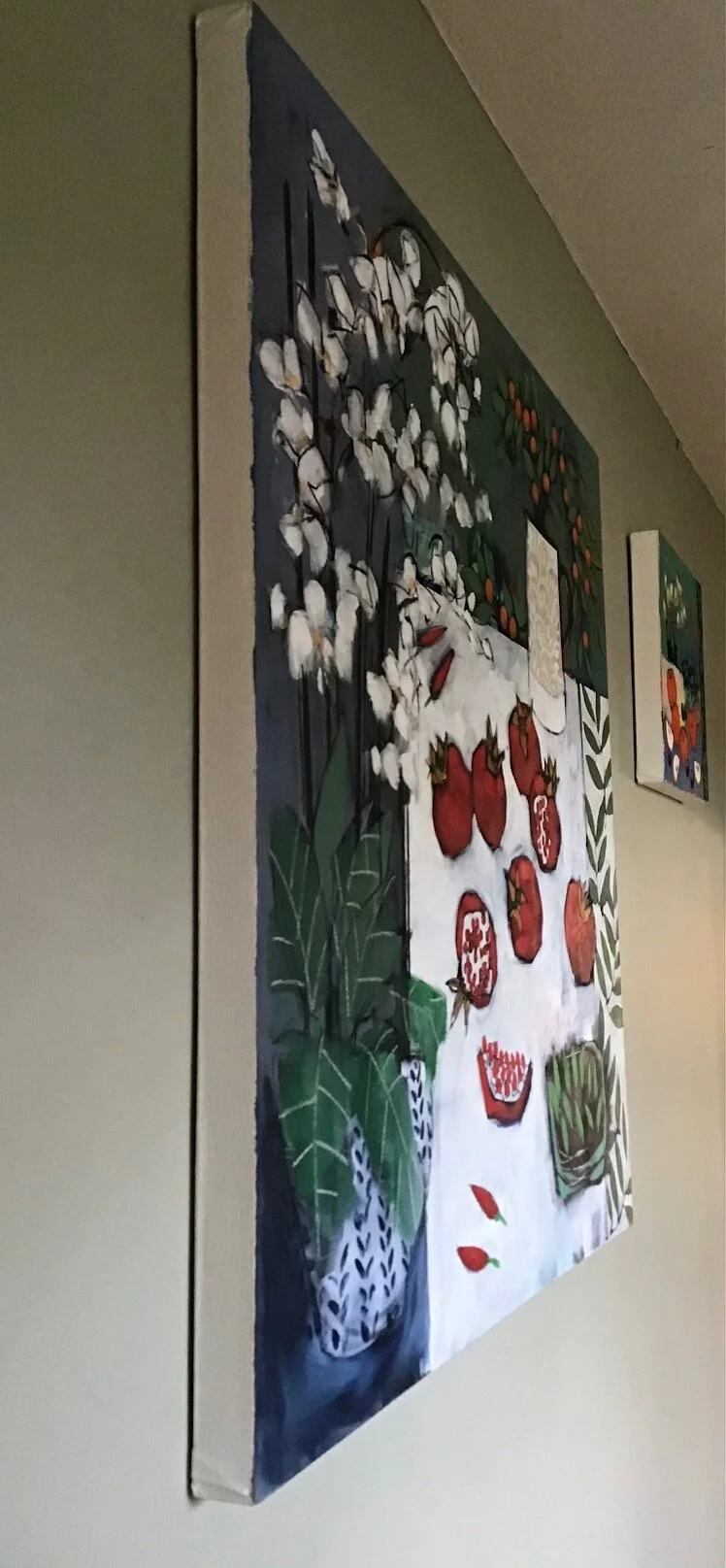 Colorful painting of a table with pomegranates, leaves, and flowers, and a backdrop of cotton branches.