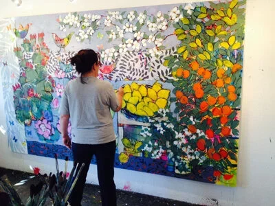 Woman painting a colorful mural on a wall filled with flowers, leaves, and abstract designs.