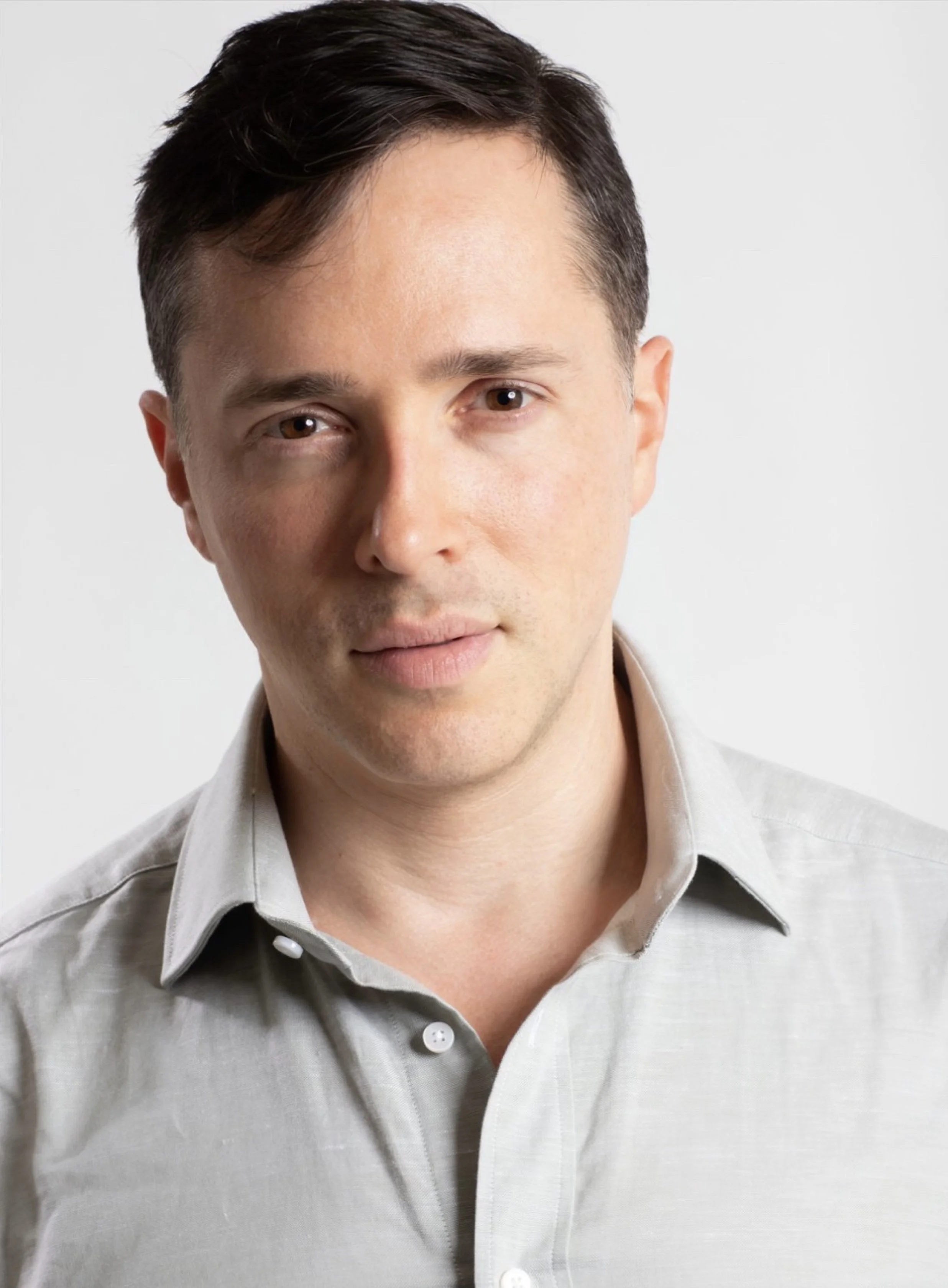 A portrait of Yuval David with short, dark hair, wearing a light-colored button-up shirt, looking directly at the camera with a neutral expression, against a plain white background.