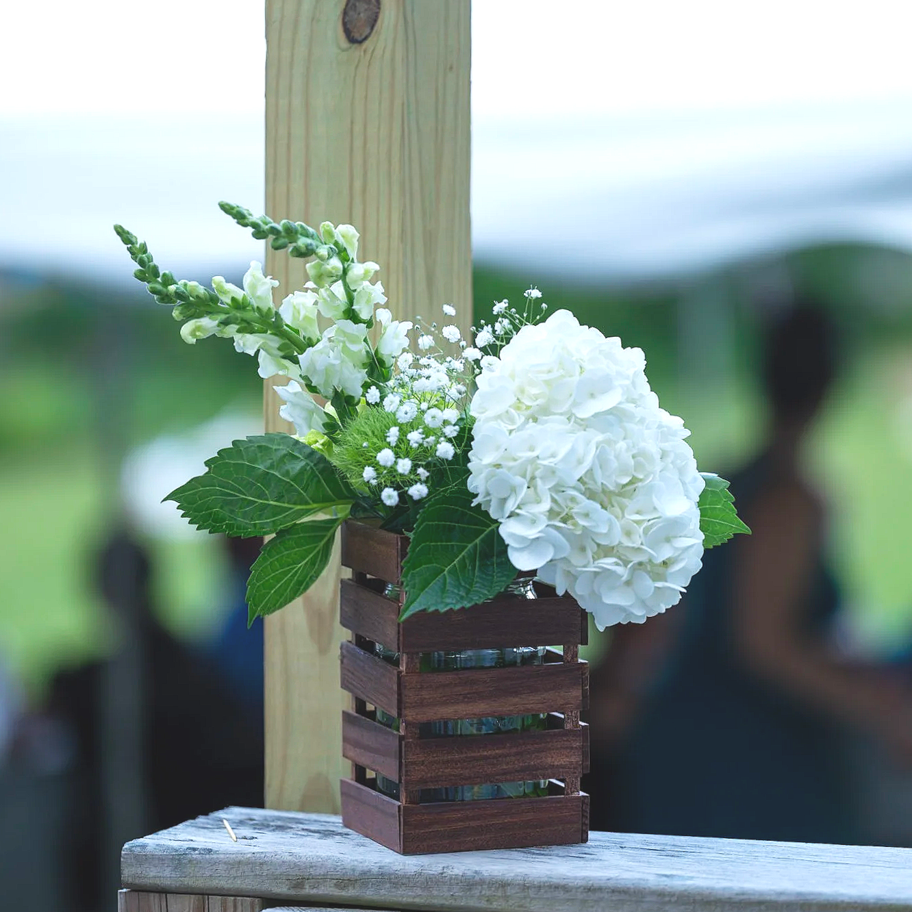 White hydrangea and small white flowers in a wooden basket on a weathered wooden ledge with a blurred outdoor background.
