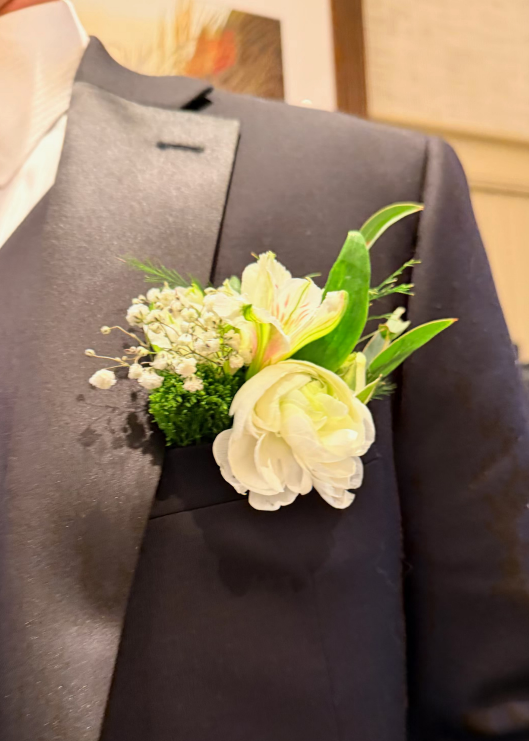 A black suit jacket with a boutonniere pinned to the lapel, consisting of white and pale pink flowers and green foliage.