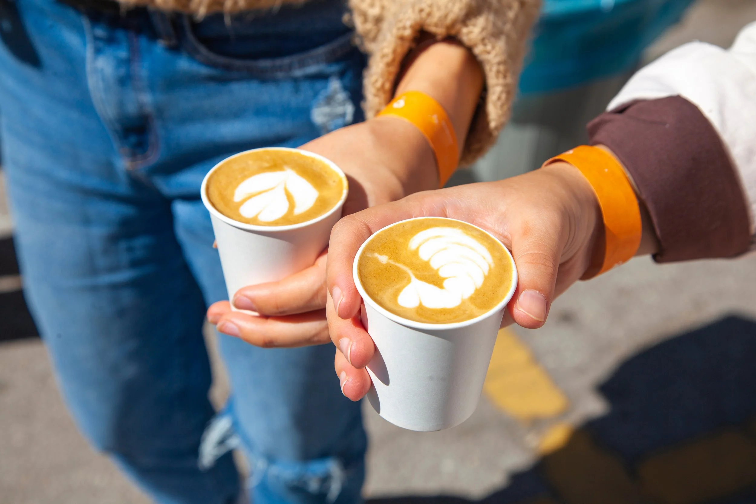 Two people holding cups of latte with leaf and tulip latte art.