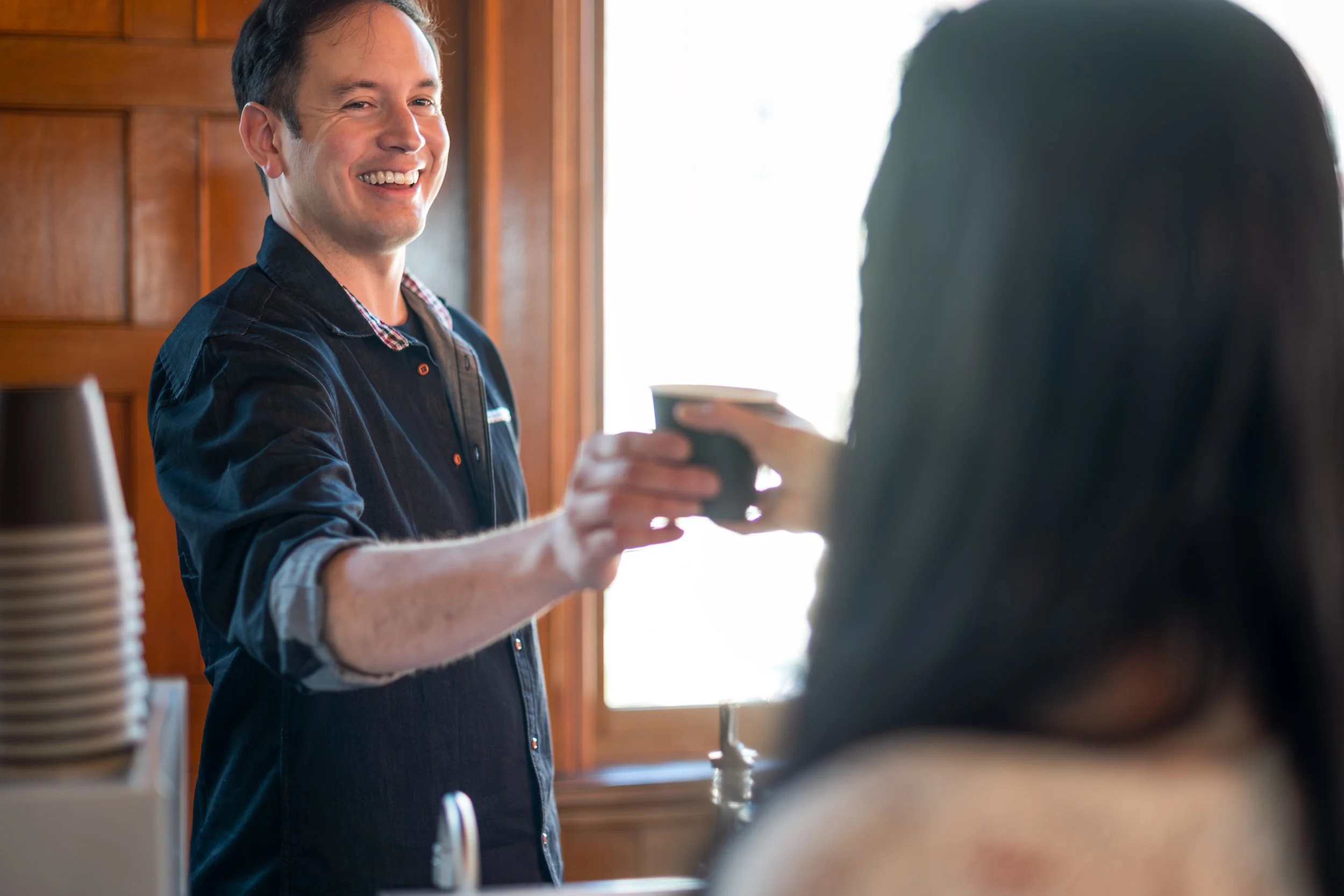 Owner Mark Pape of Preamble Coffee Cart Catering in Fort Wayne, Indiana smiling as he serves a hot latte to a happy woman at a private event.