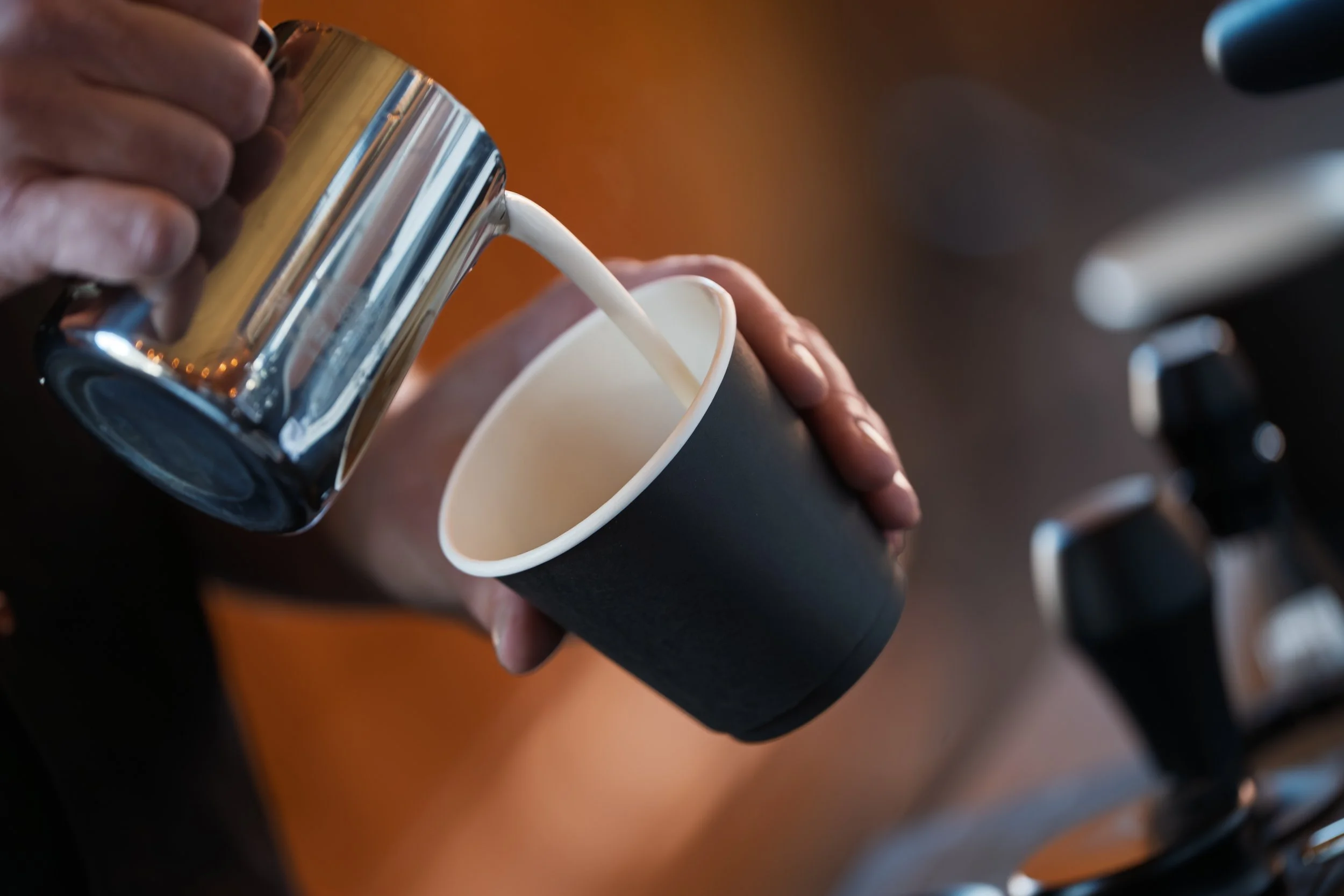 A barista with Preamble Coffee Cart in Fort Wayne, Indiana expertly pouring milk into espresso to create a latte with beautiful latte art for a guest.