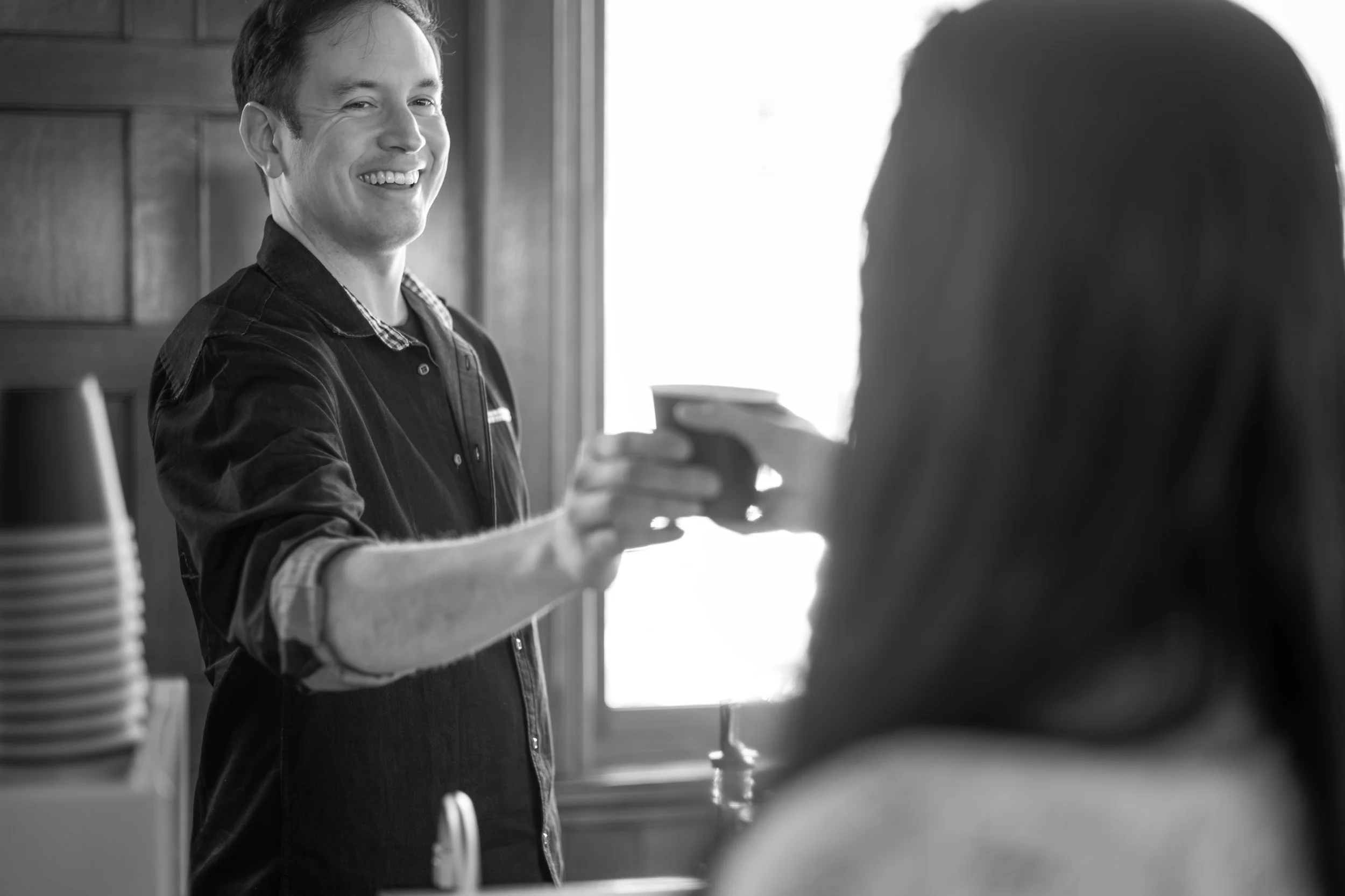 A young man as a barista is smiling as he serves a woman the latte that she ordered from Preamble Coffee, at an event where customers enjoyed espresso drinks.