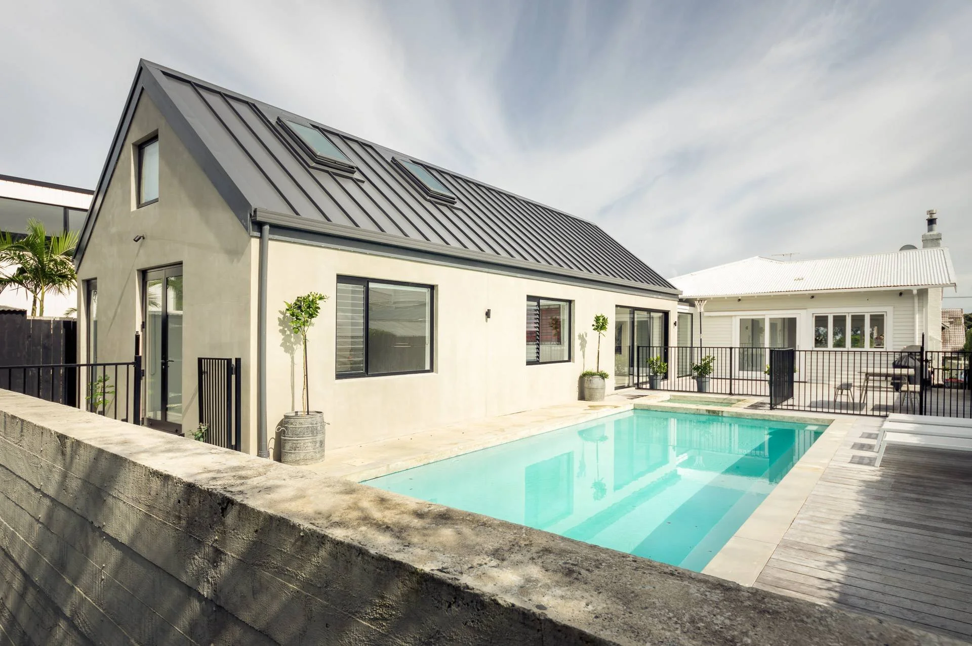 Modern house with a backyard swimming pool, potted plants, and a wooden deck.