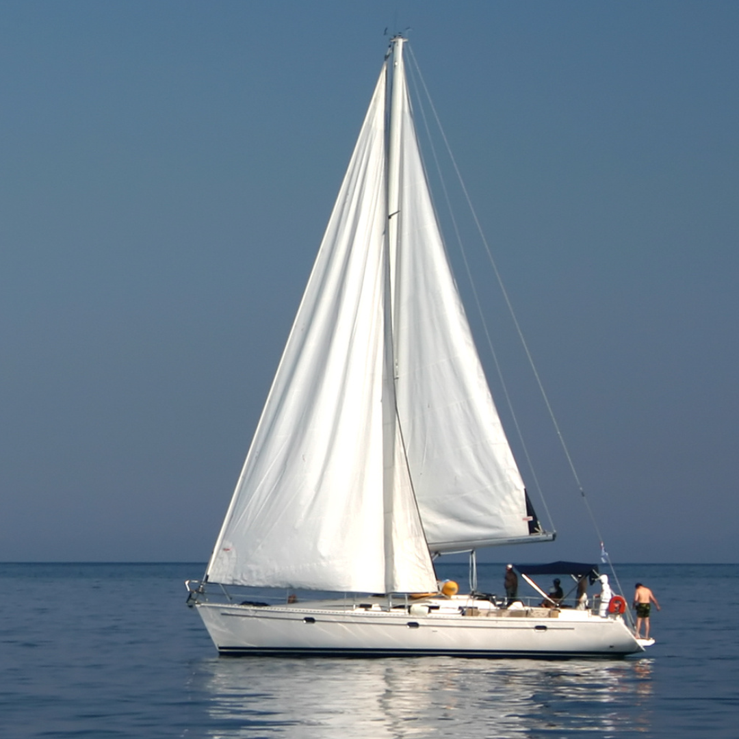 A sailboat with white sails on calm blue water, with several people on board and at the stern, under a clear sky.
