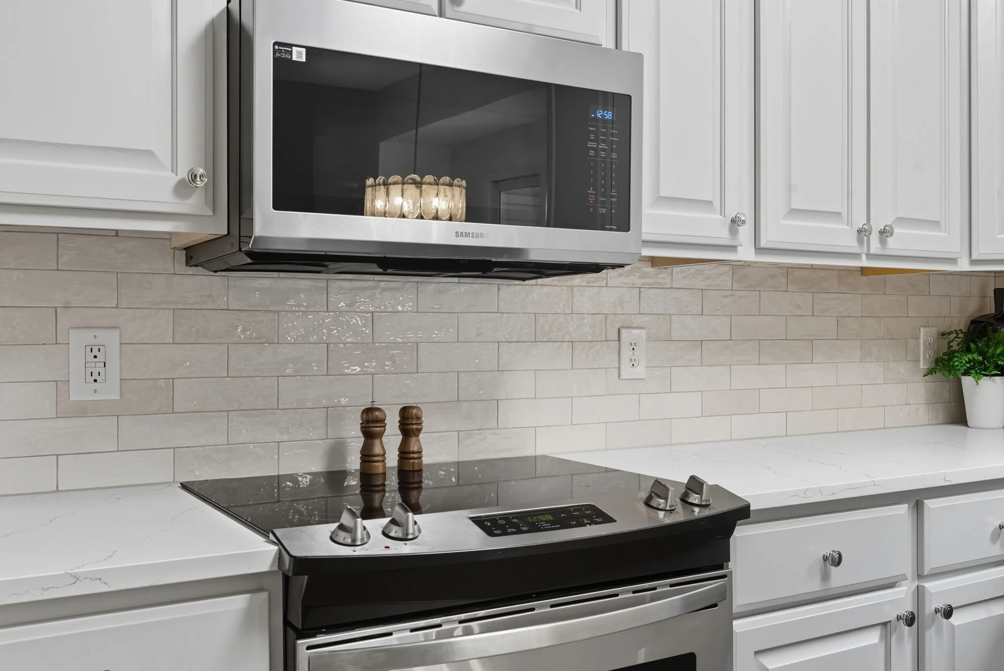 Kitchen with white cabinets, stainless steel microwave, black stovetop with two spices, and a white countertop with a plant on the right