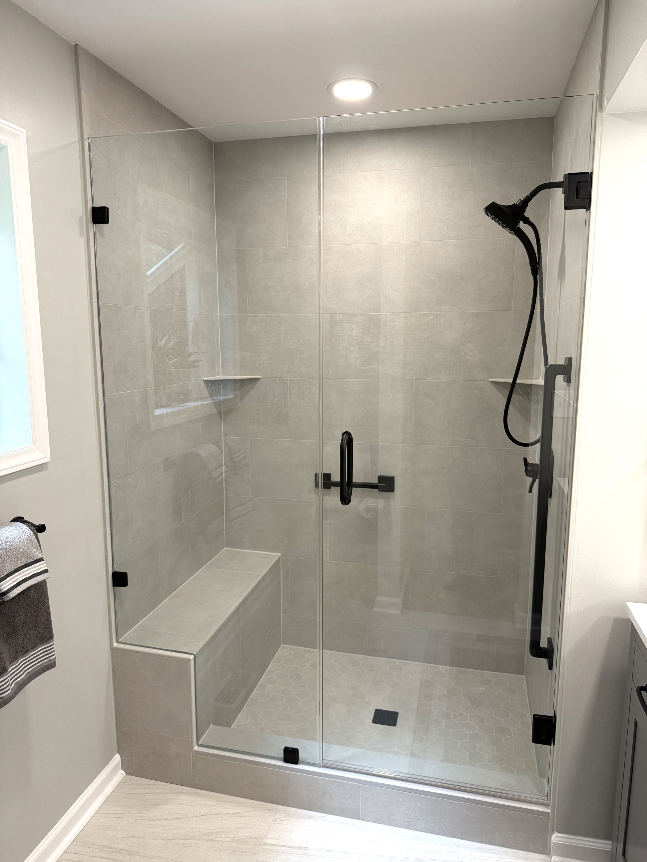 Modern glass shower stall with black hardware, a built-in tiled bench, and a rainfall shower head.
