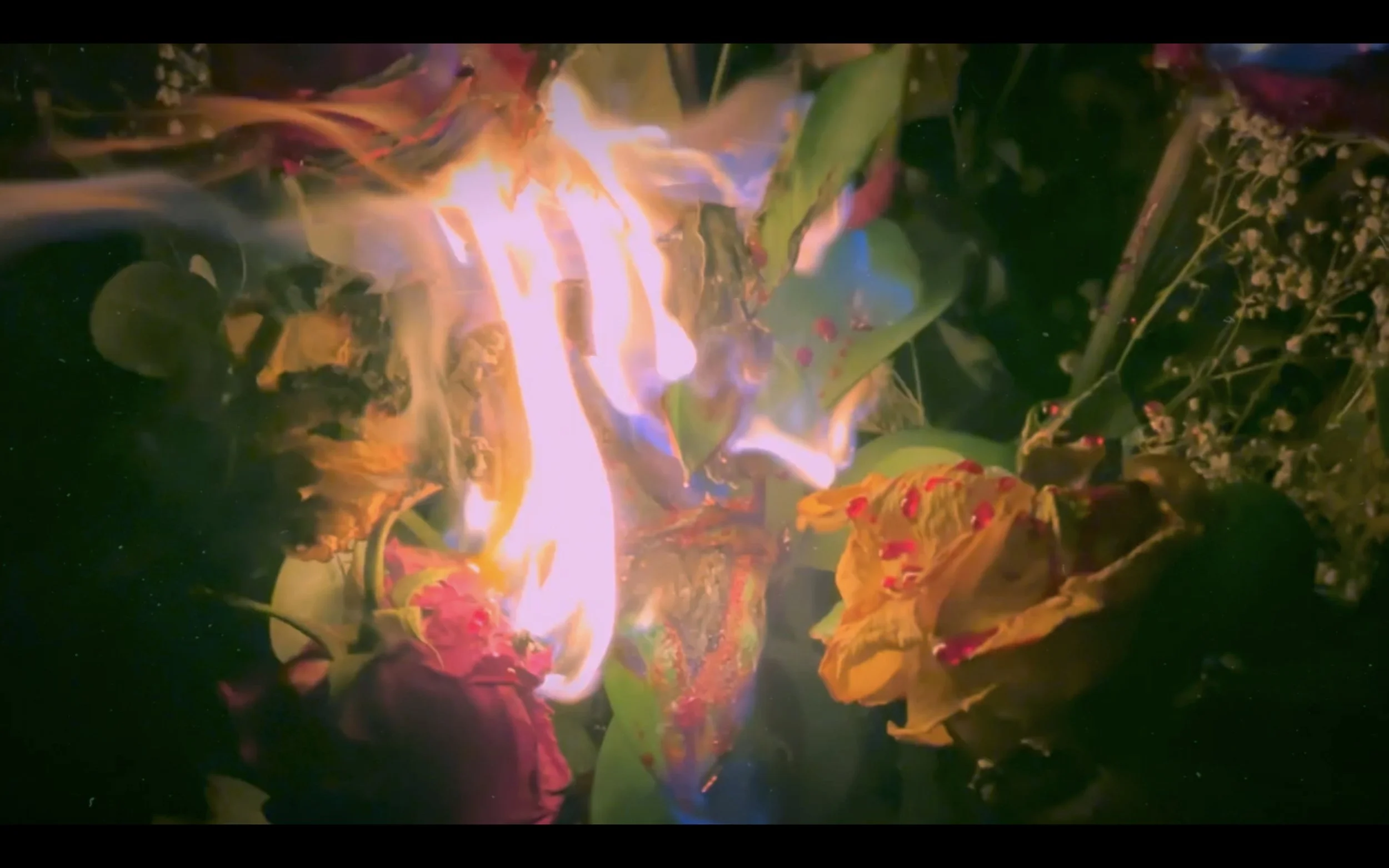 A ceremonial fire with colorful flowers and green leaves surrounding it, possibly part of a ritual or religious offering.