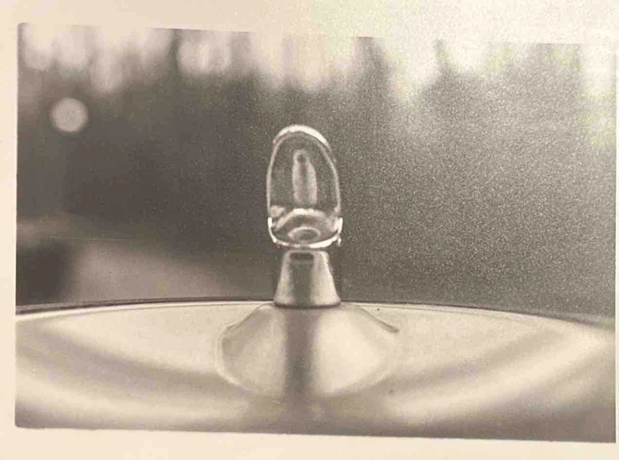 Close-up of a droplet on a metallic surface, reflected and magnified, with a blurred background.