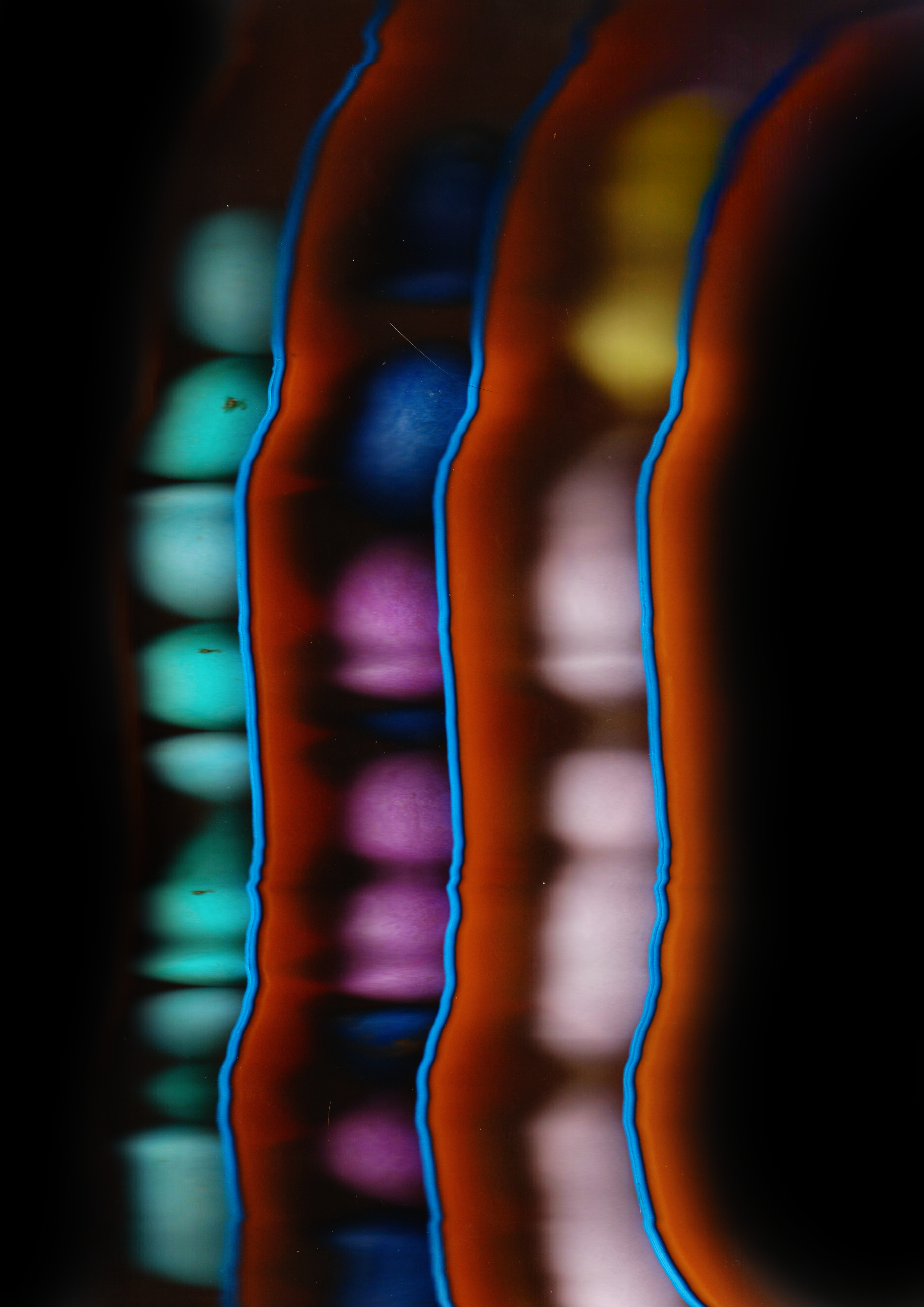 Close-up of colorful glowing light trails forming wavy vertical lines on a dark background, creating an abstract pattern.