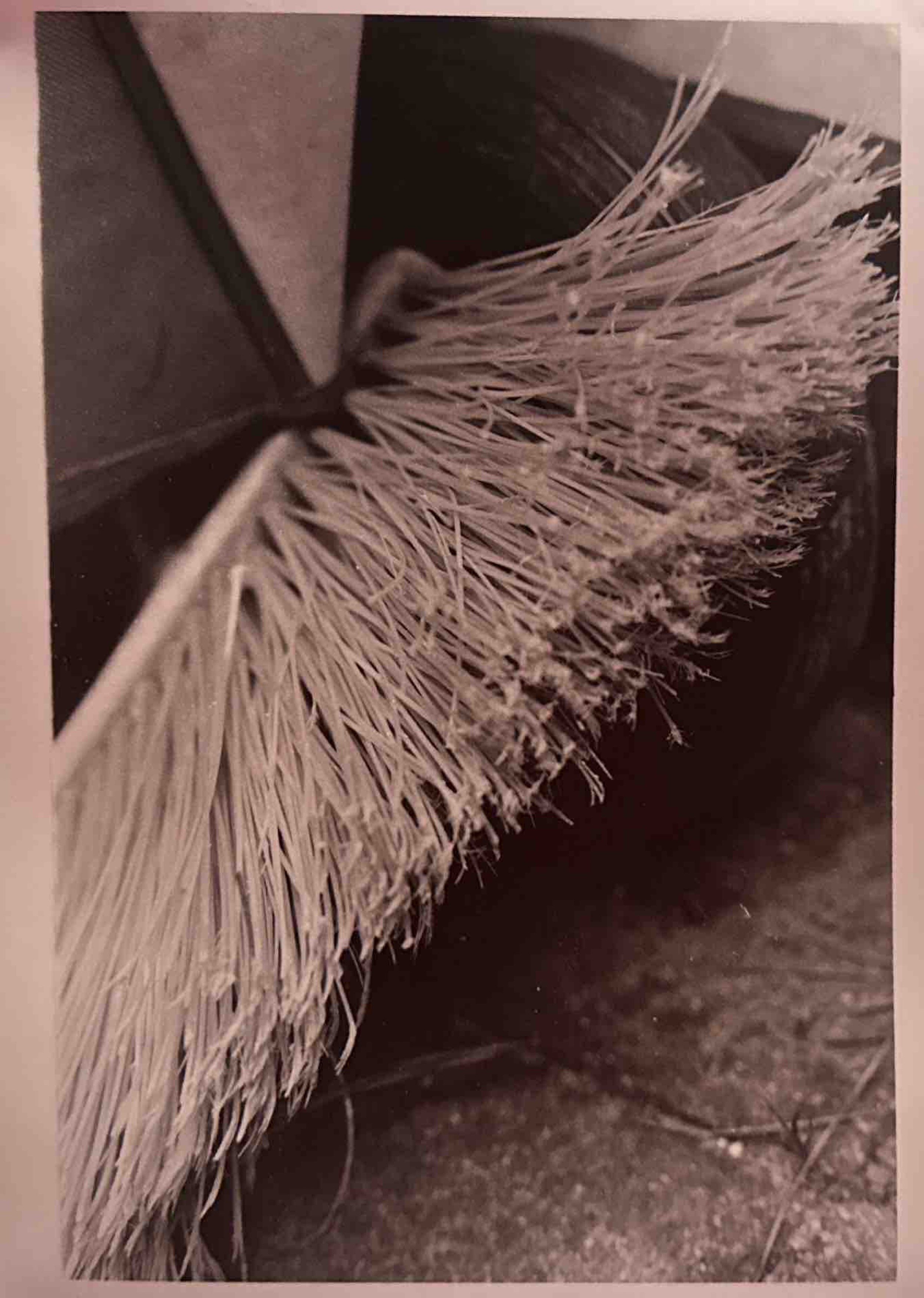 Close-up of a worn broom with frayed bristles resting on a surface.