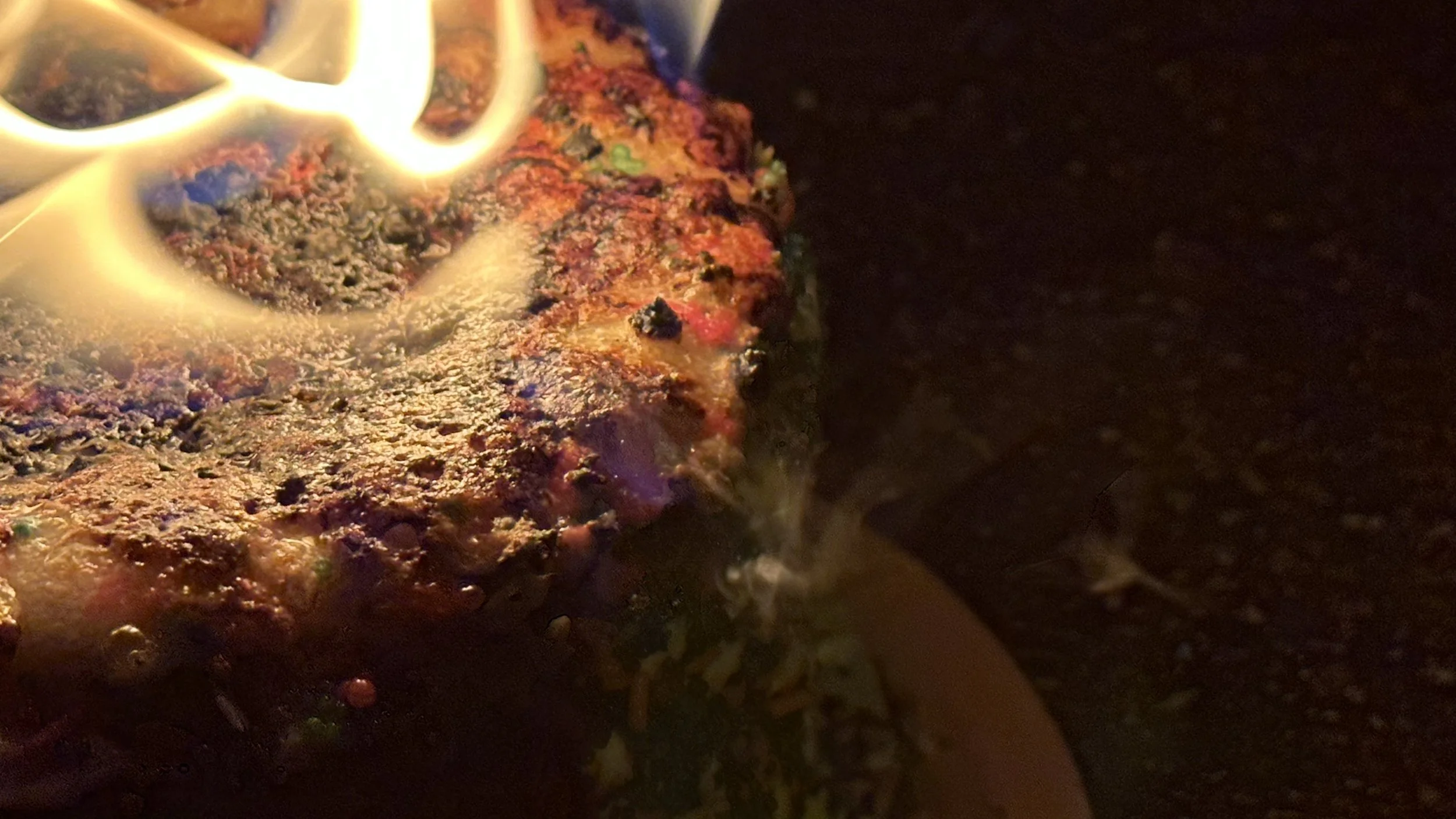 Close-up of a burger patty sizzling on a hot skillet with small cups of condiments or sauces in the background.