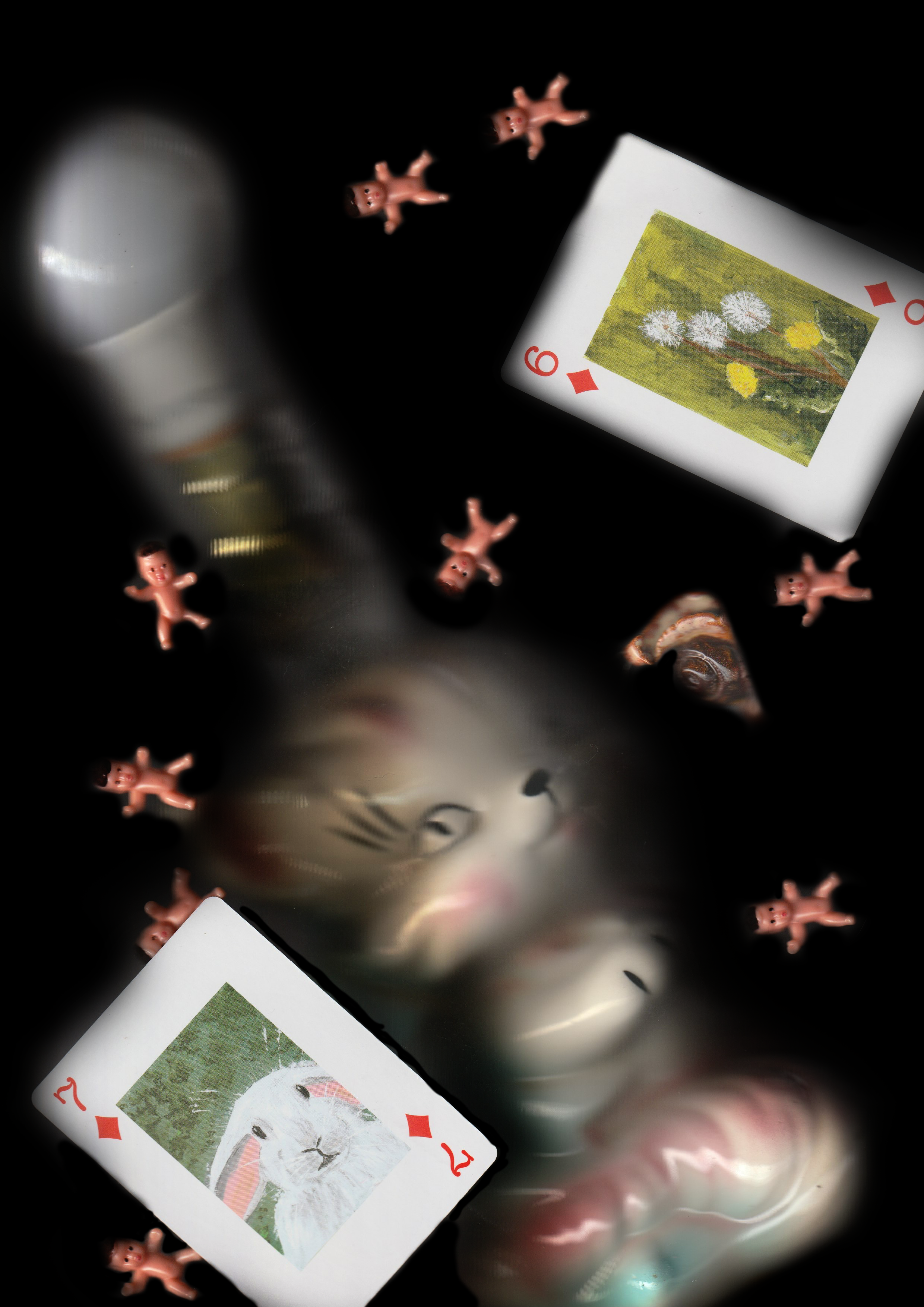 A surreal composition with a fish's face, playing cards featuring rabbits and flowers, small pink dolls, and a blurred bottle against a dark background.