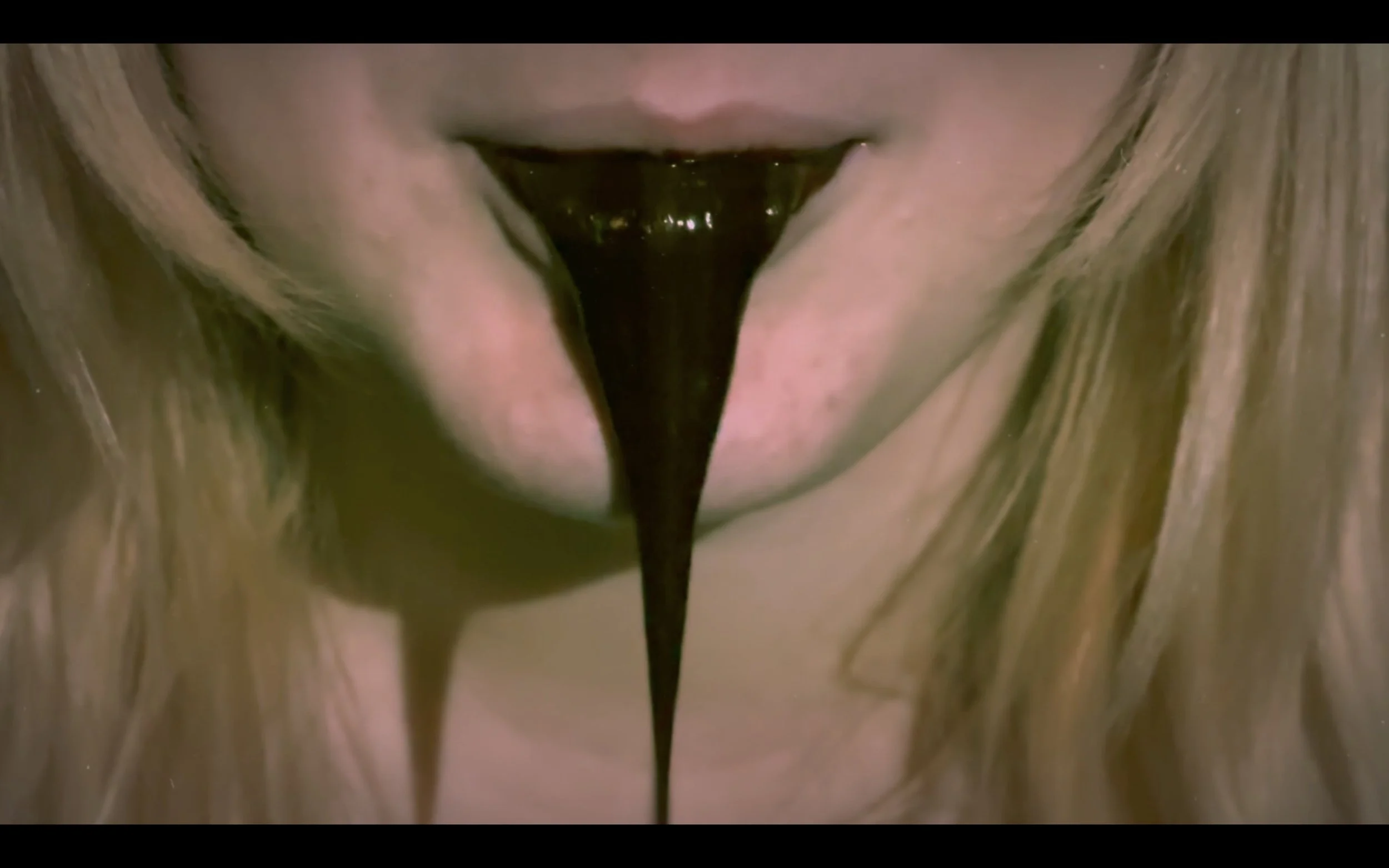 Close-up of a person's open mouth with black liquid dripping from the tongue.