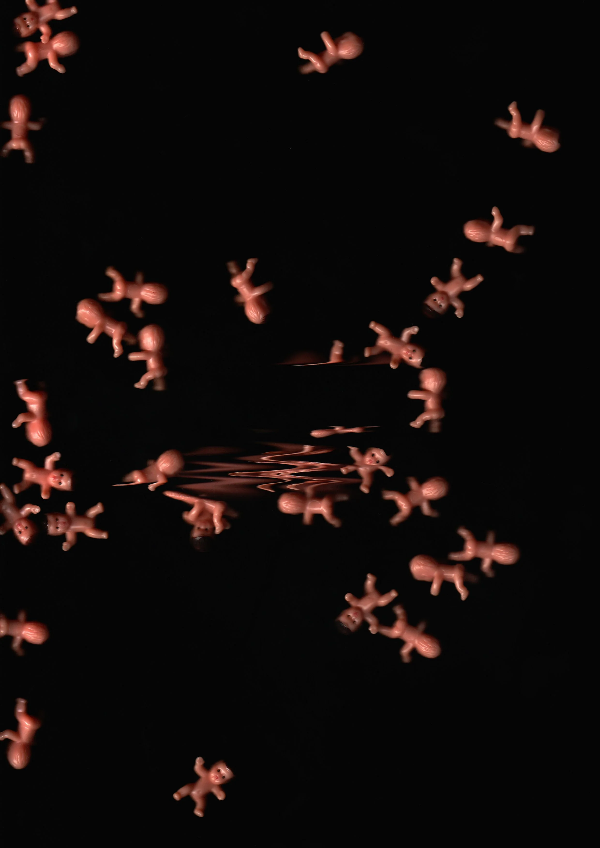 Small pink plastic dolls are scattered and floating on a black reflective surface, creating a mirror-like reflection.