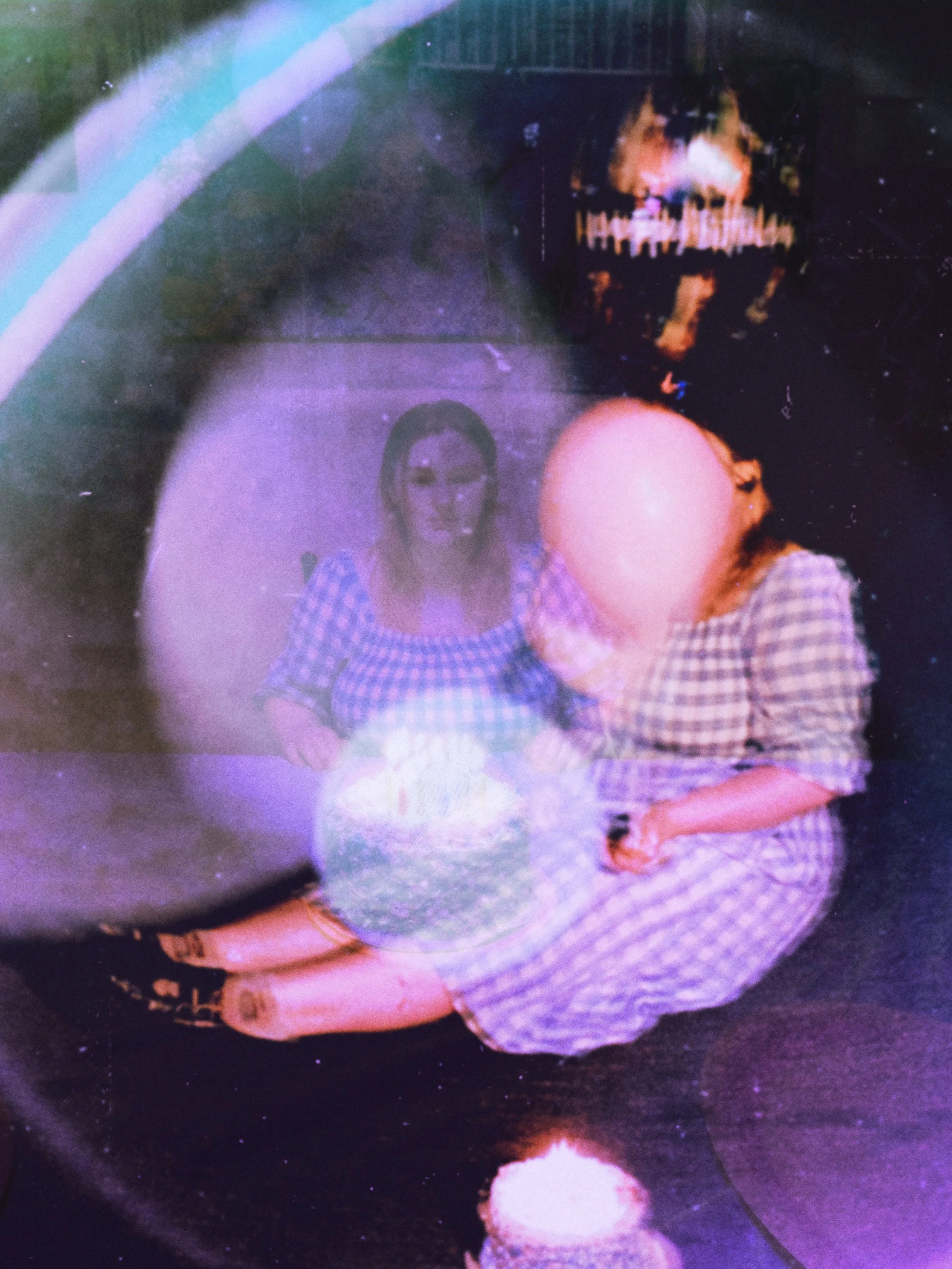 A woman and a person with a bald head wearing plaid clothing, sitting on the floor with a birthday cake in front of them, celebrating a birthday.