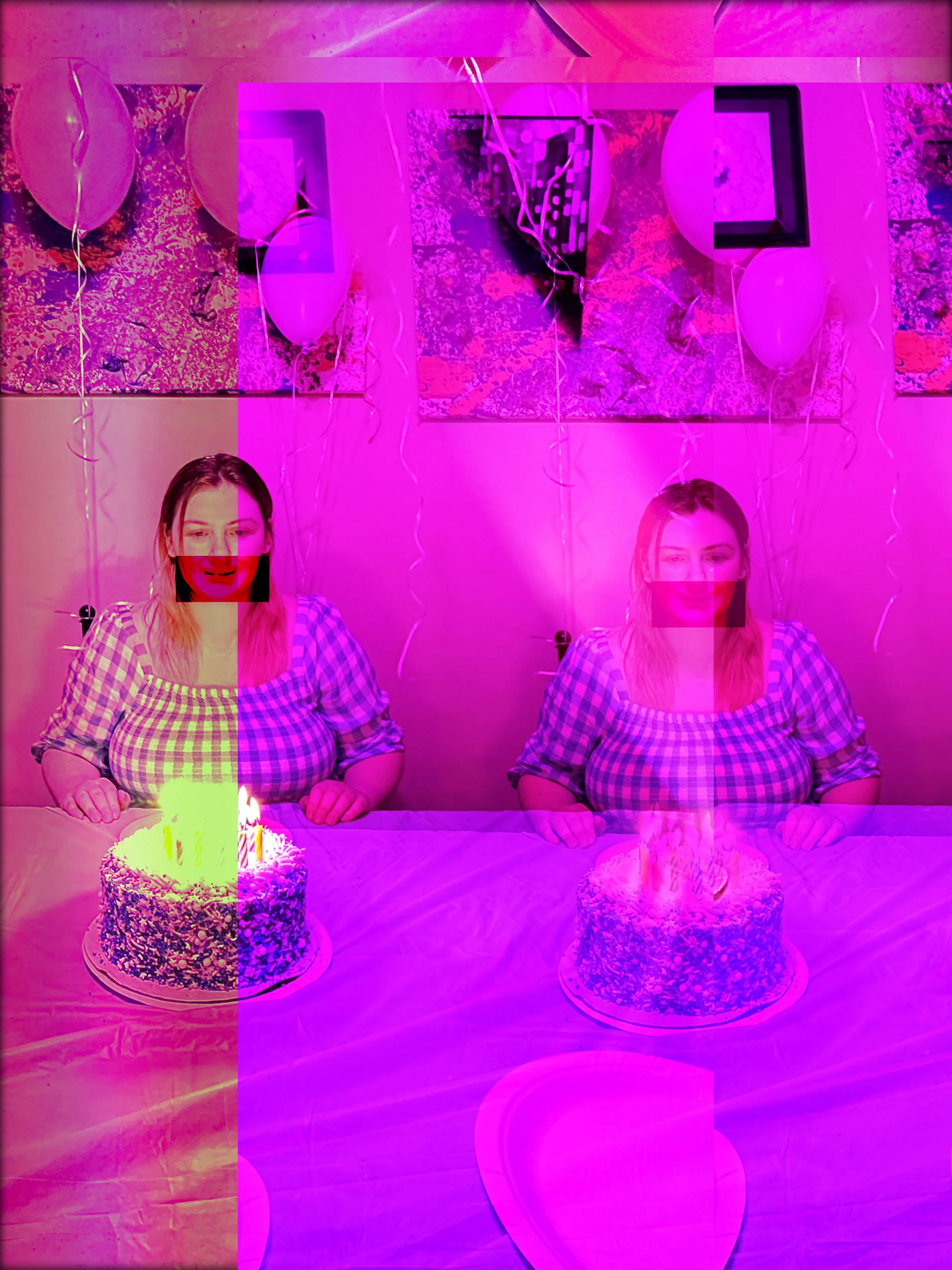 A woman sitting at a table with two birthday cakes with lit candles, decorated with balloons and balloons on the wall, with pink and purple lighting.