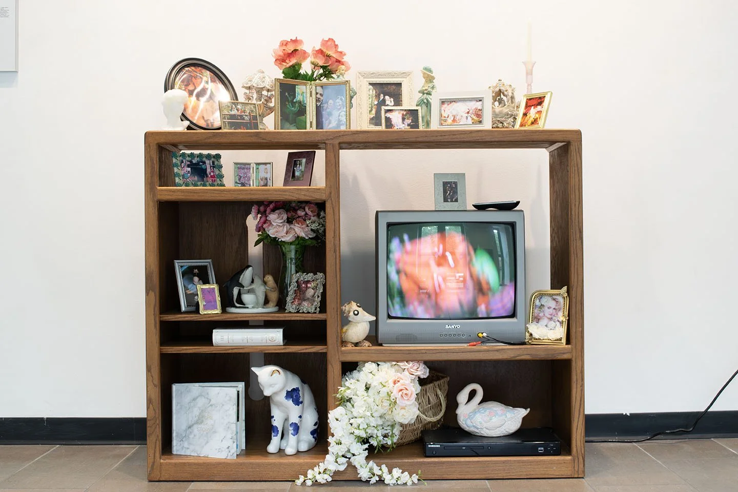 Wooden entertainment center with a small television, framed photos, decorative items, flowers, and ornaments.
