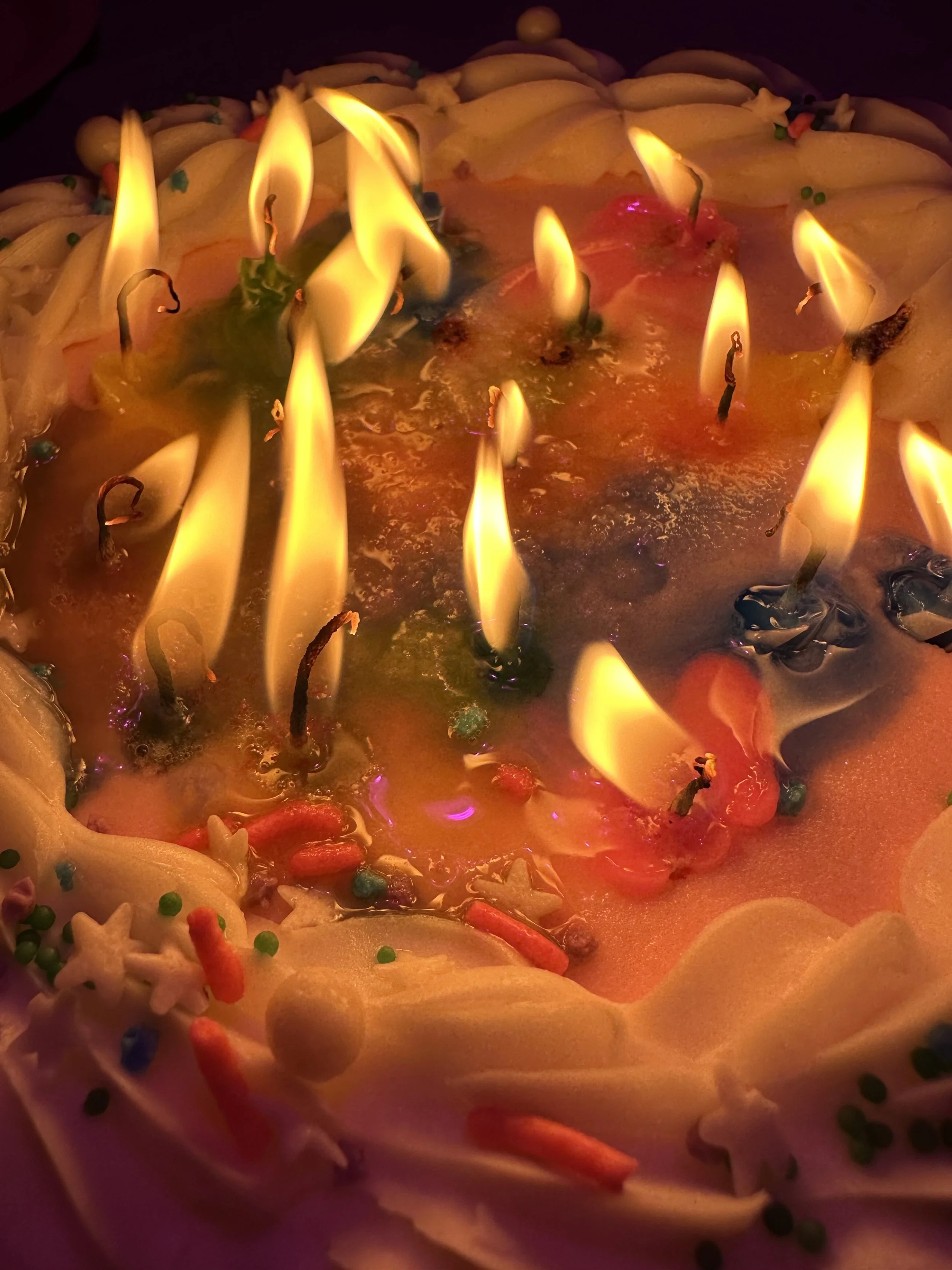 A birthday cake with multiple lit candles and colorful sprinkles.