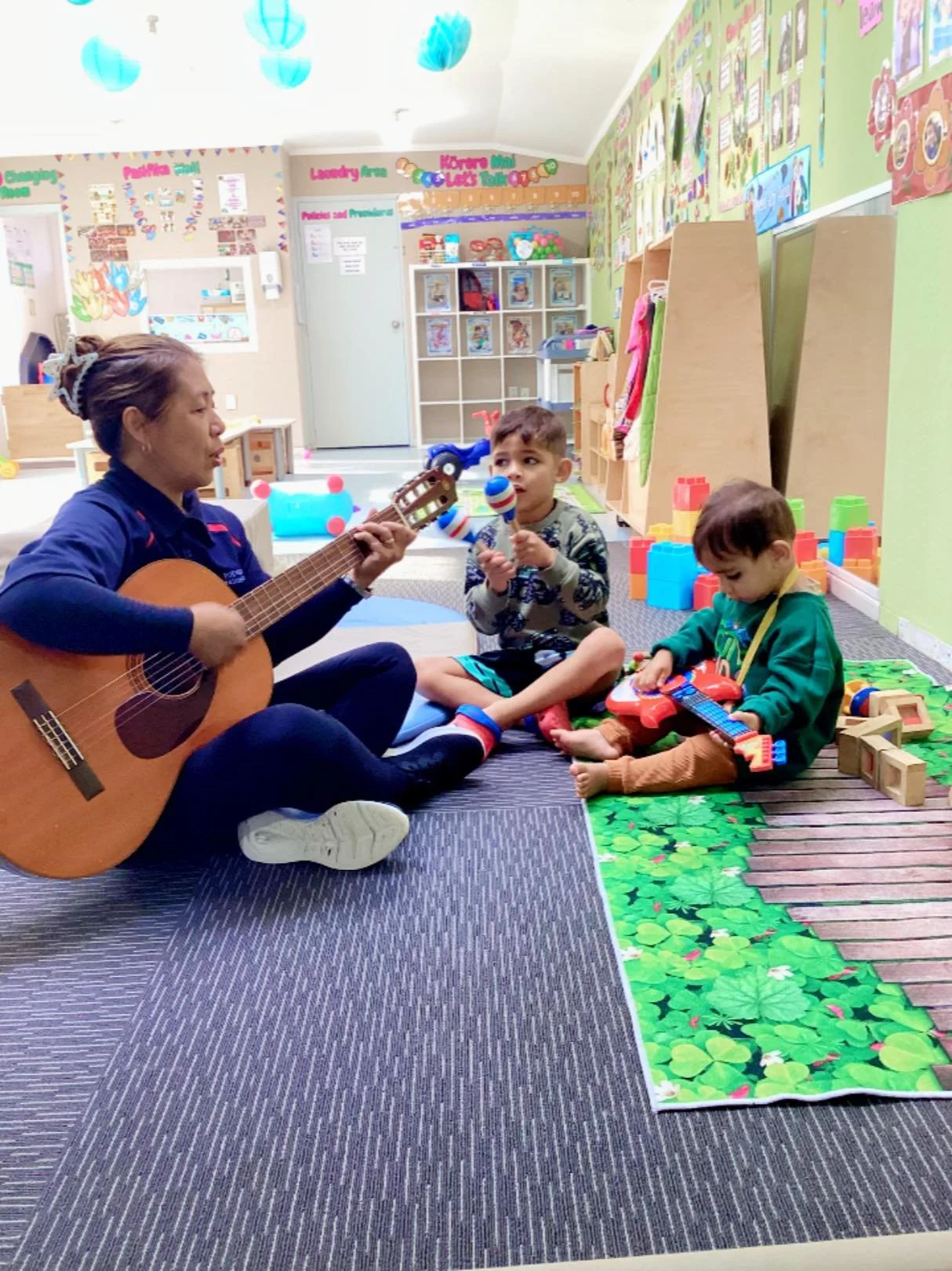 Pukeko Preschools Claudelands kids with teacher playing guitar
