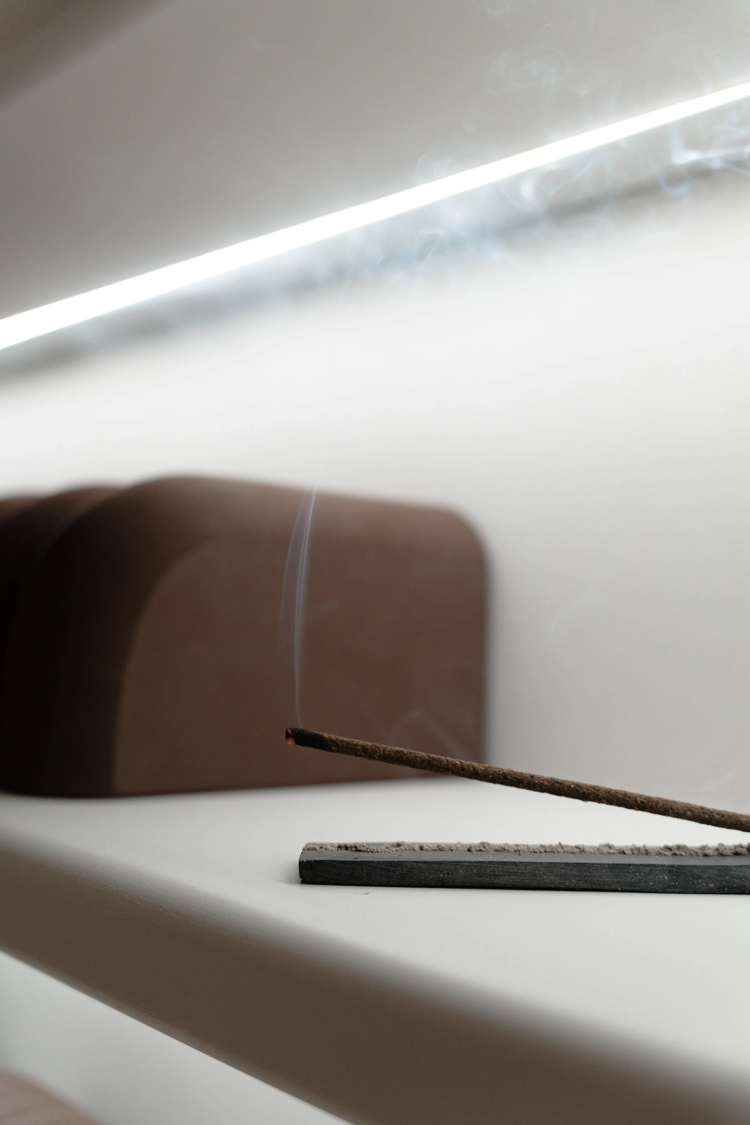 Close-up of incense stick burning on holder with smoke rising.