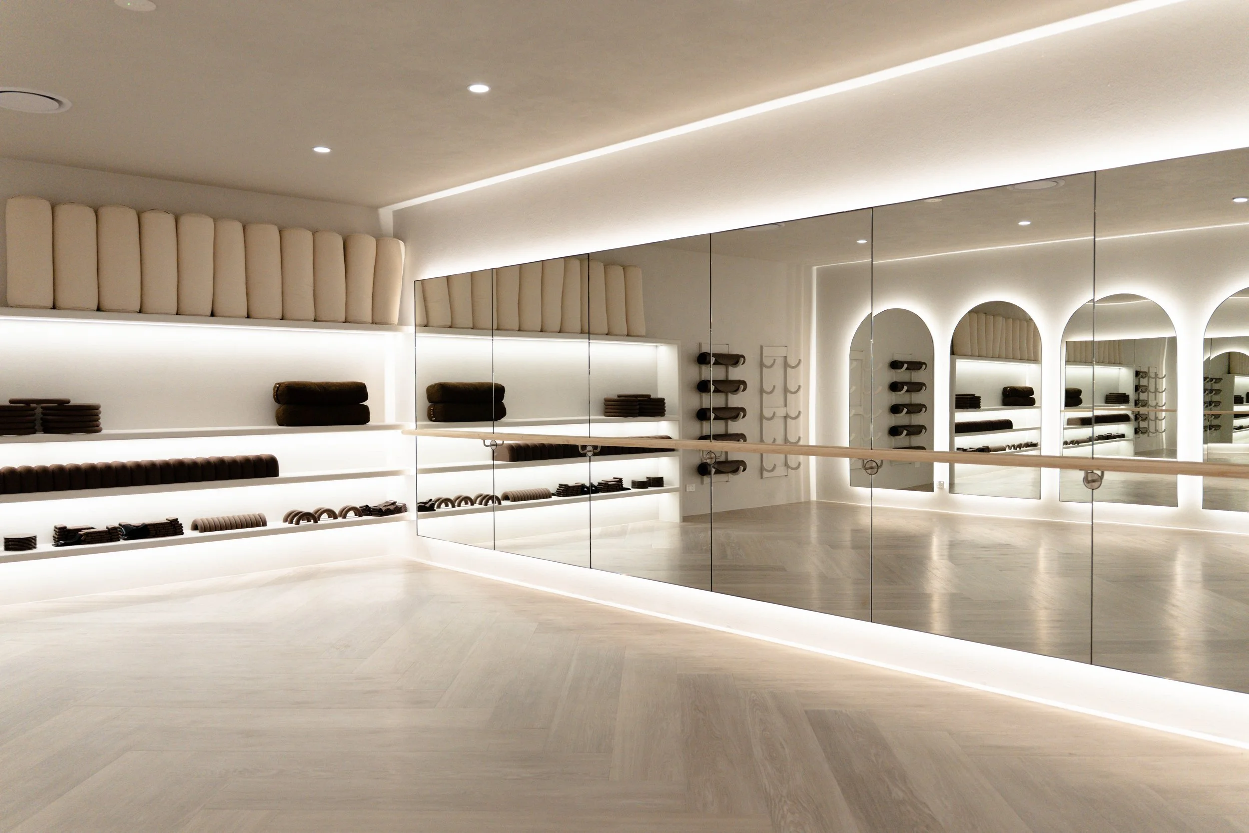 Modern clothing store interior with shelves displaying folded clothes and accessories, mirrored wall, beige floor, and ceiling with recessed lighting.