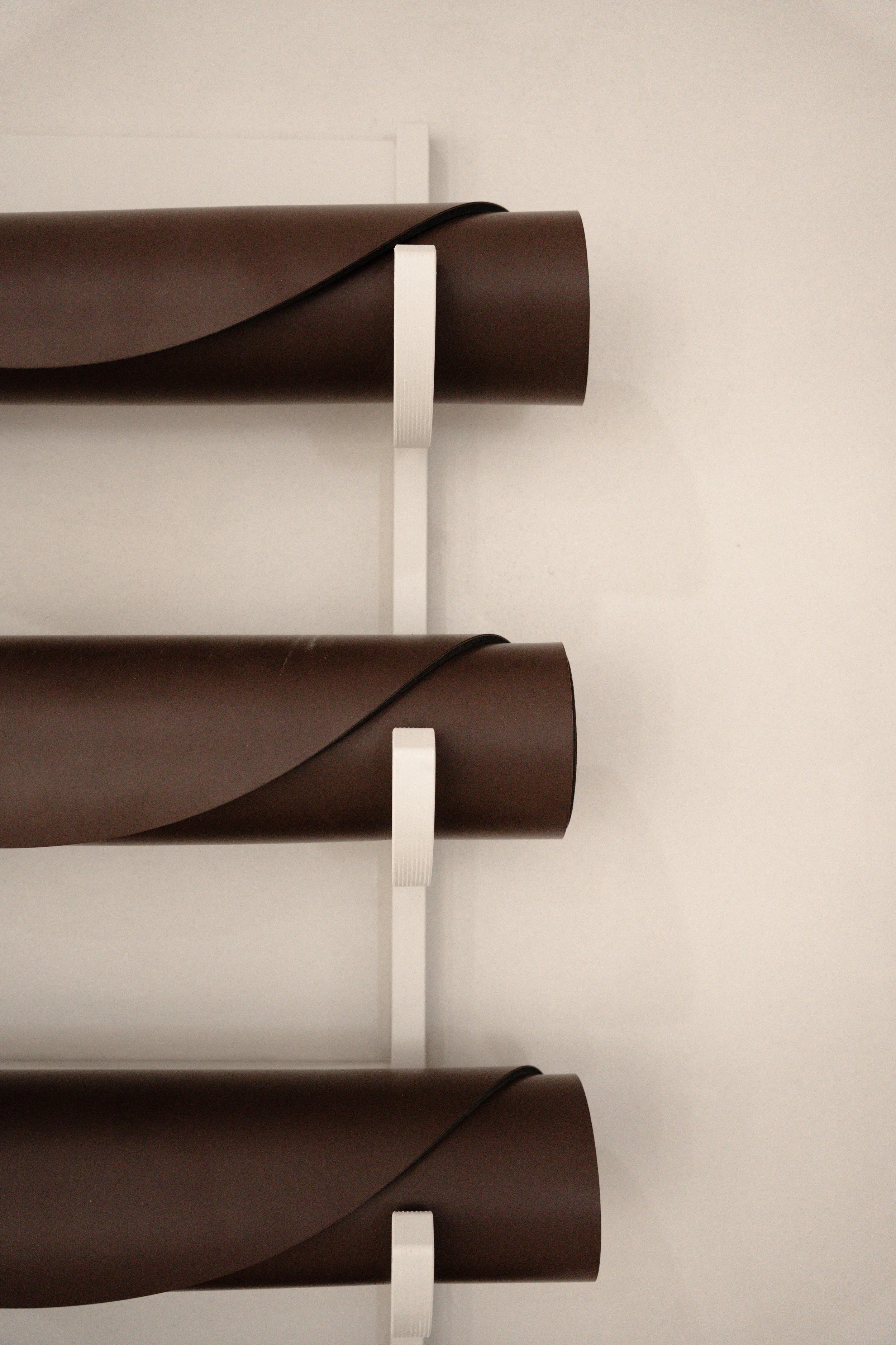 Stack of three dark brown rolled-up papers or fabric rolls mounted on a white wall with white brackets.