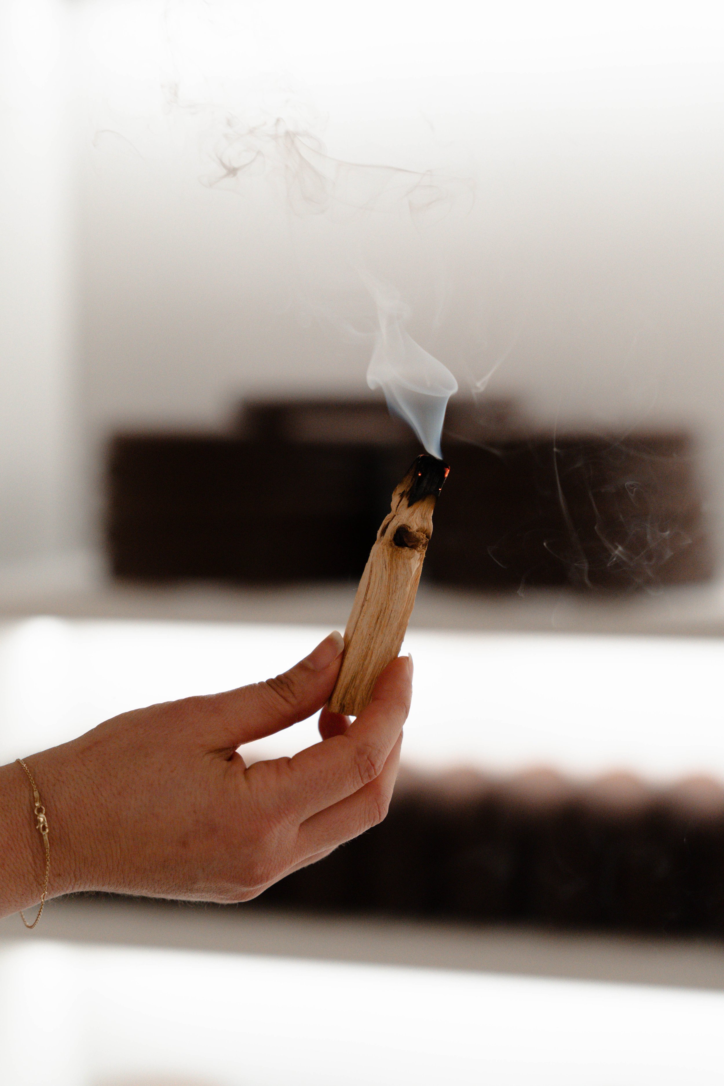 A person holding a lit matchstick with a small flame and smoke, blurred background.