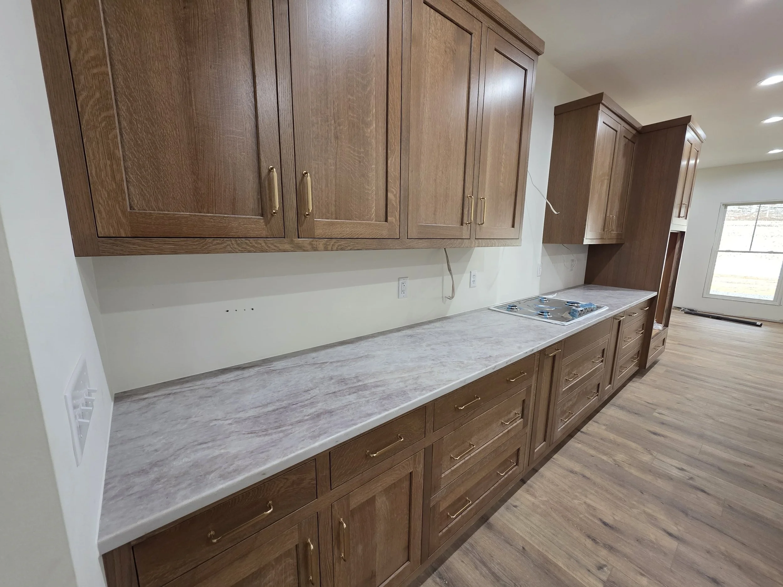 Kitchen with wooden cabinets, marble countertop, and an electric cooktop, spacious with hardwood floors and a large window in the background.
