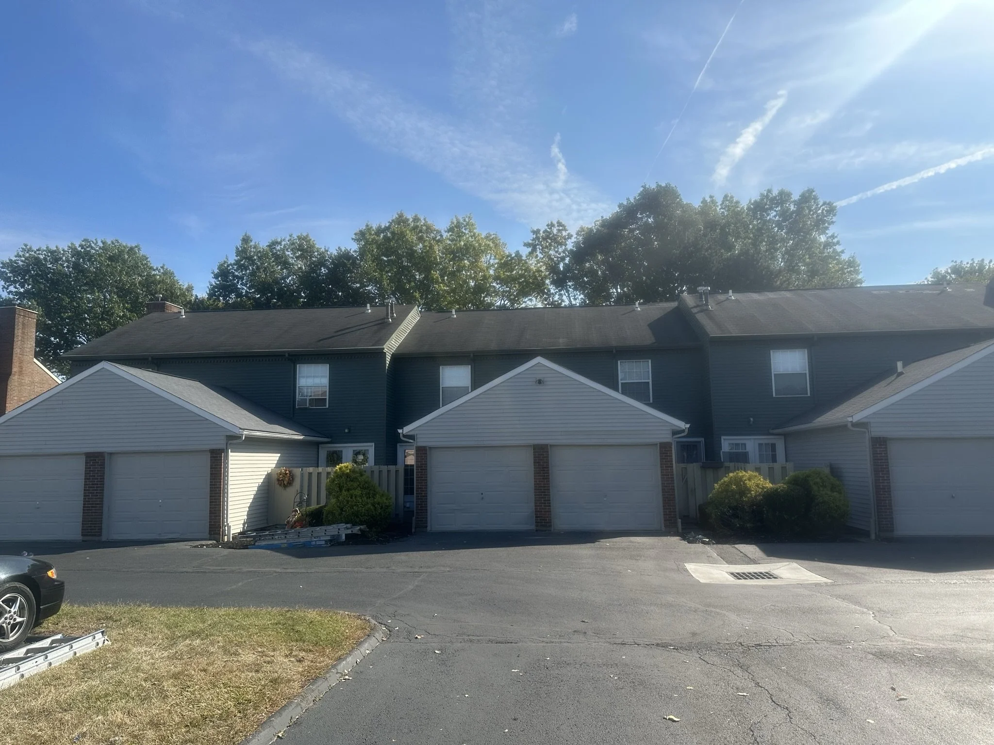 View of a residential apartment complex with attached garages, trees in the background, a clear blue sky, and a parking lot in the foreground.