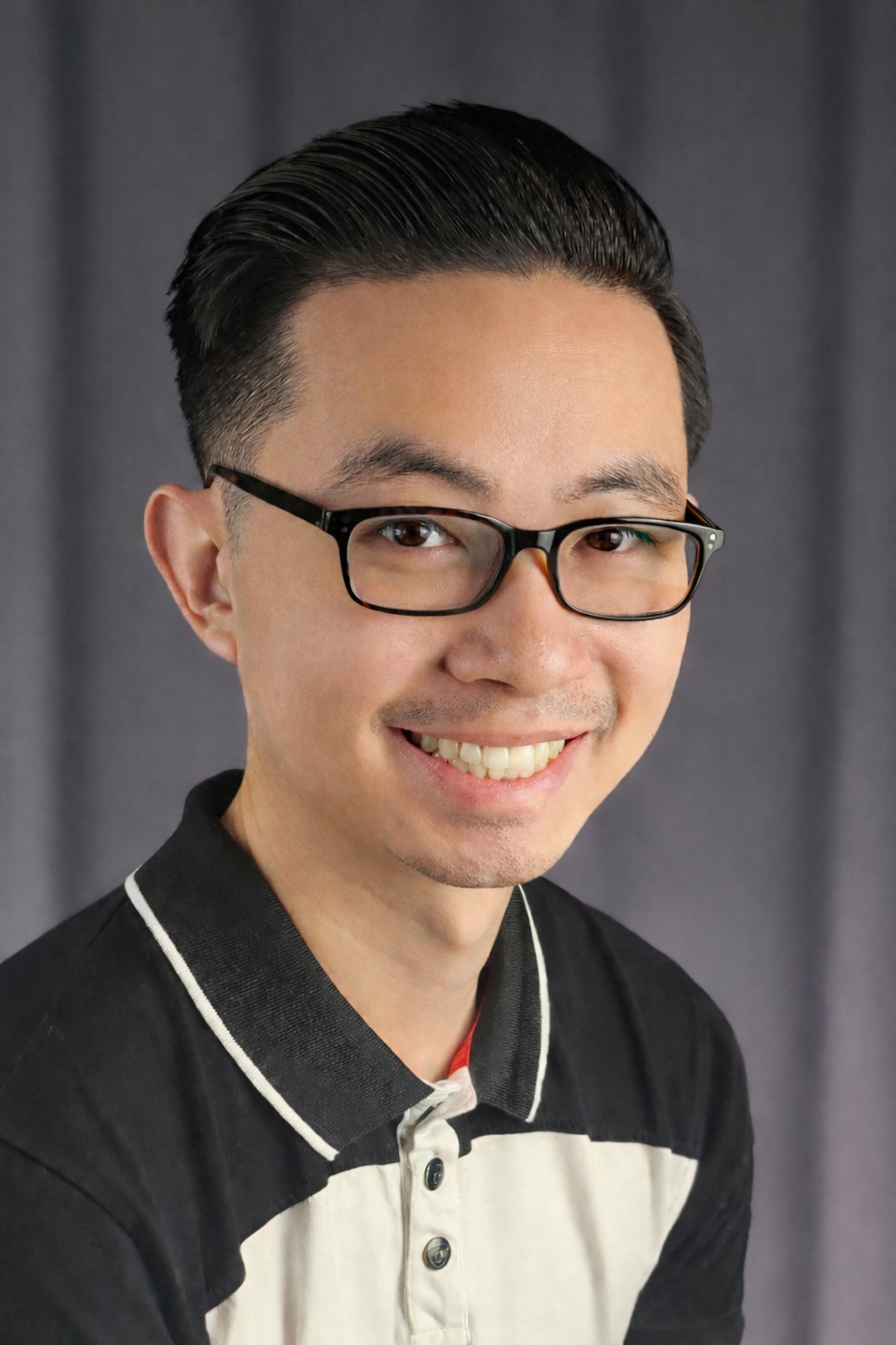 Smiling man with black glasses, slicked-back hair, and wearing a black and white collared shirt.