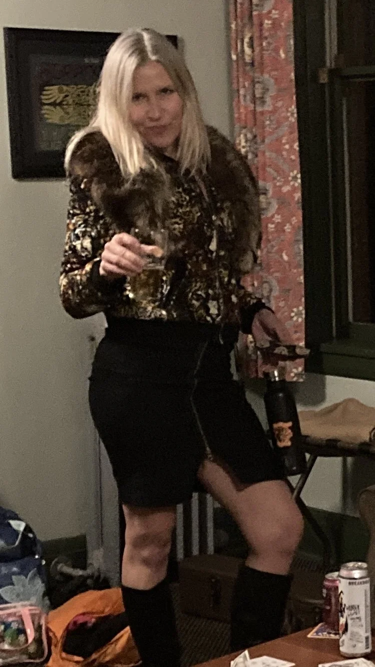 A woman with blonde hair holding a brown and black patterned dog, standing next to a table with drinks, in an indoor setting.