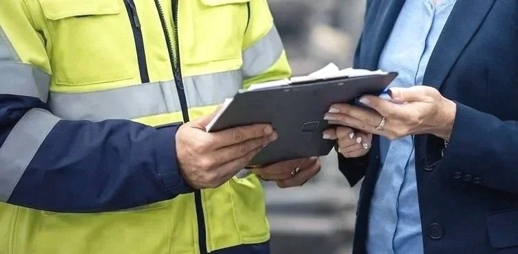 Two people examining a clipboard together outdoors, one in a high-visibility jacket and the other in a suit.