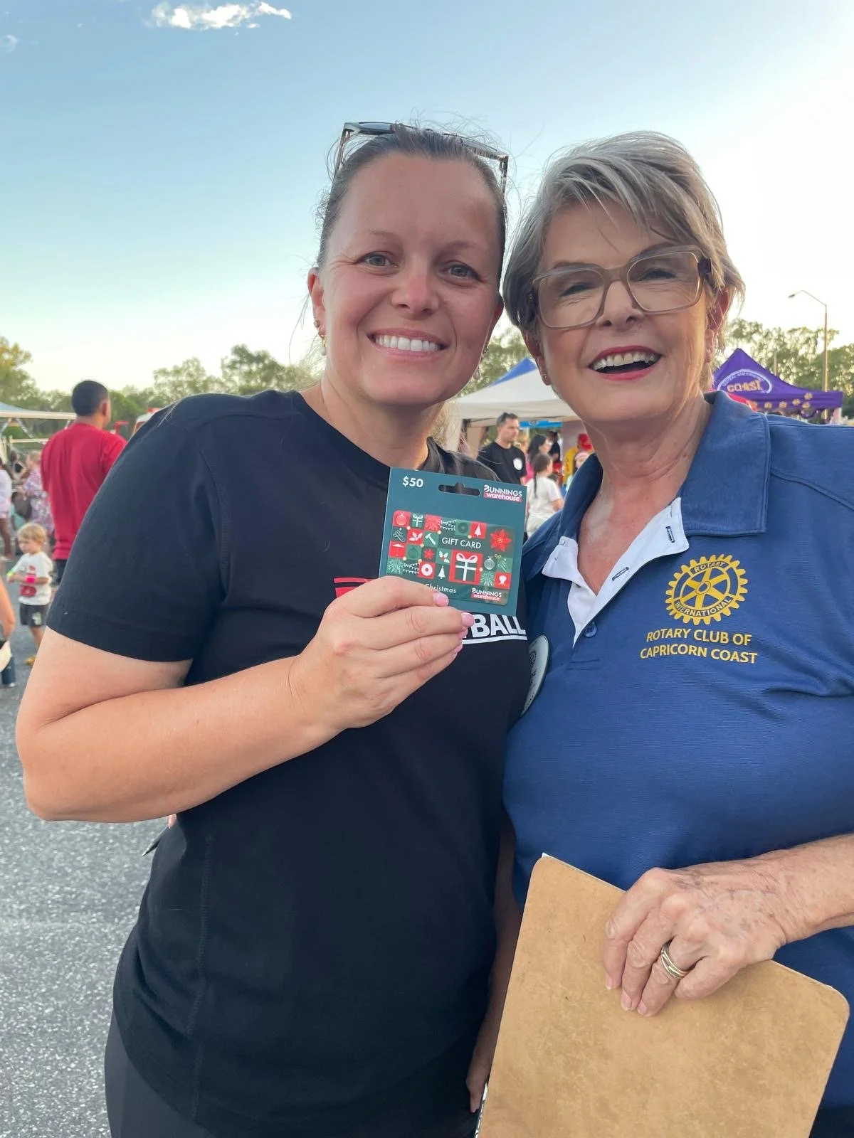 A young woman holds up a Bunnings giftcard while posing with a the female 2025 Rotary presidemt