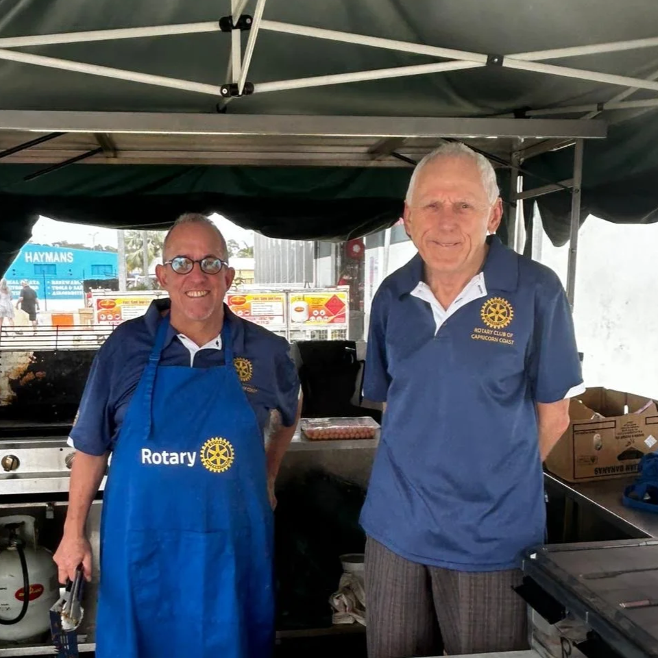 Photo of smiling Rotary Members grilling sausages
