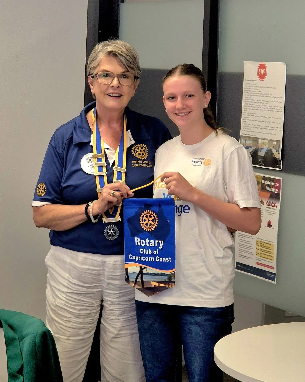 female Rotary Club president holds a blue Rotary banner with a young female exchange student