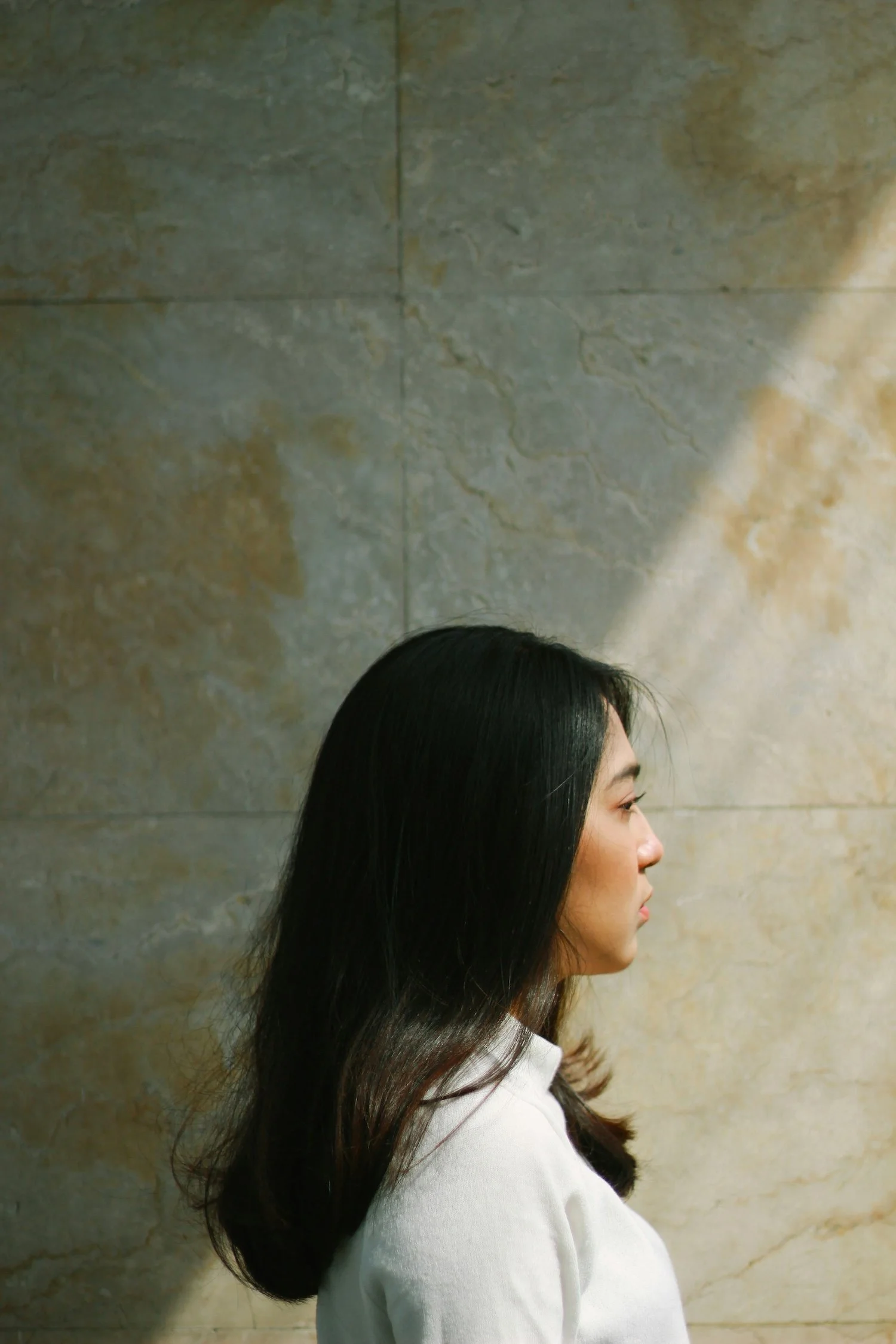 profile view of woman with dark hair and a white shirt standing against a marble background