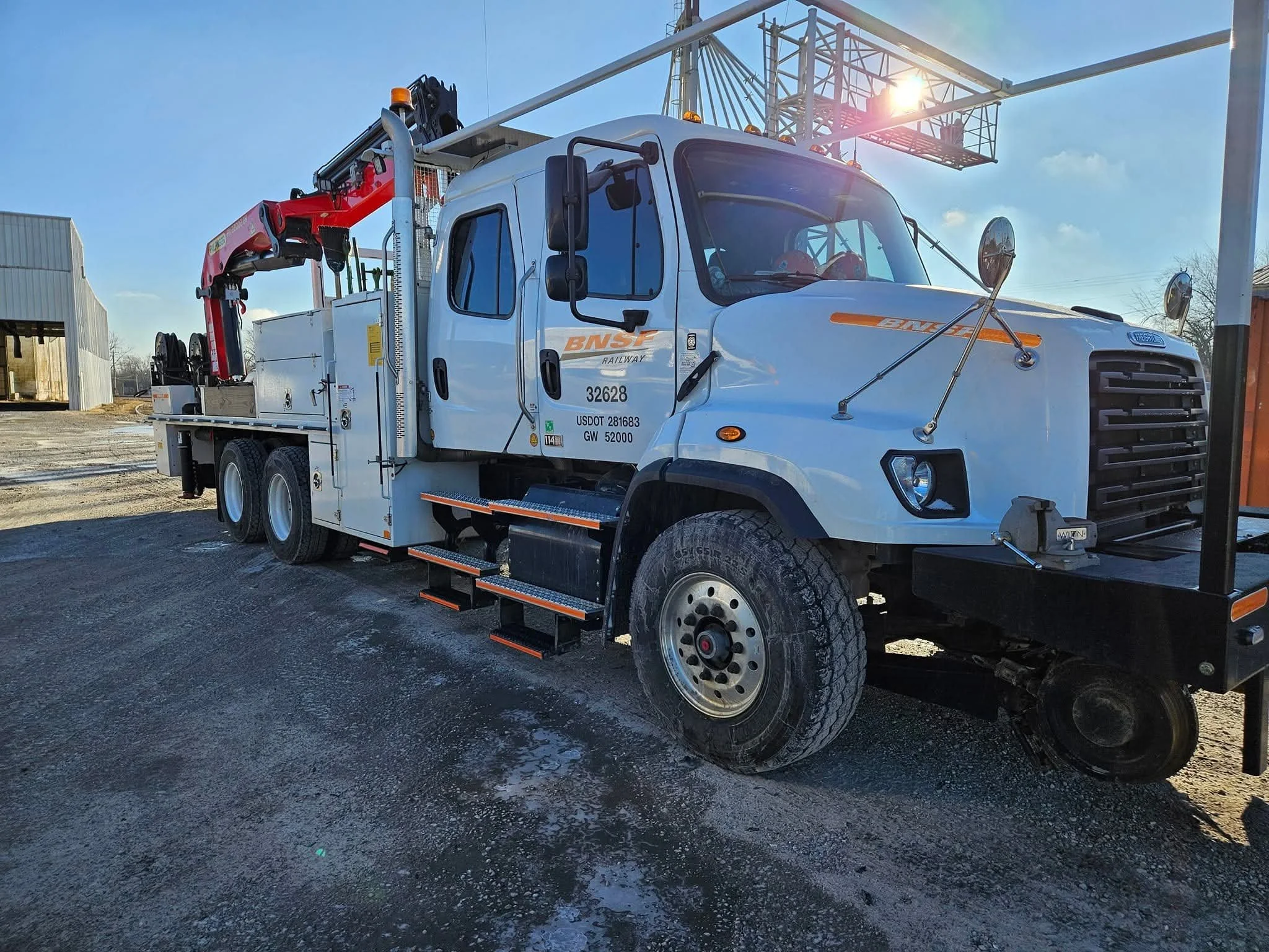 White service truck with BNSF Railway markings and a mounted crane, parked outdoors on a gravel surface.