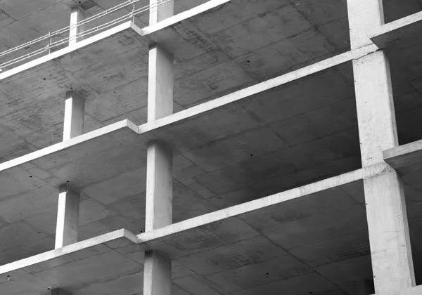 Black and white photo of an unfinished concrete building with open floors and structural beams.