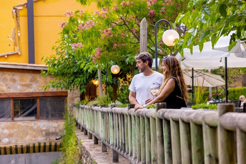 Una pareja conversando en un balcón con vegetación y faroles