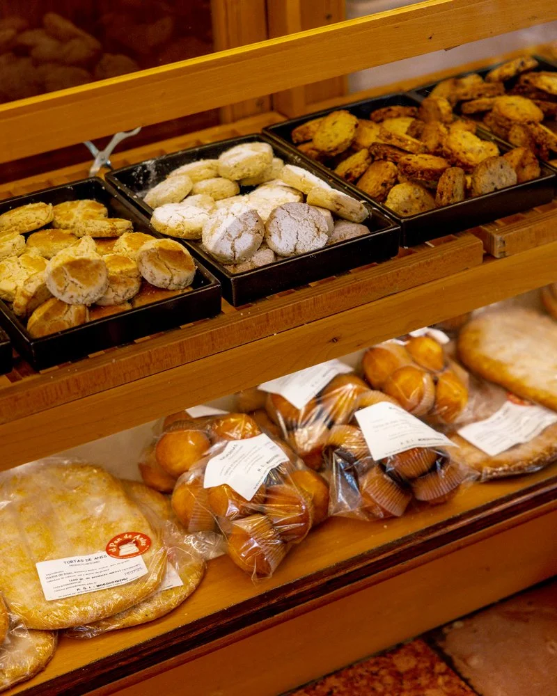 Variedad de galletas, panes y dulces en una repisa de madera en una panadería