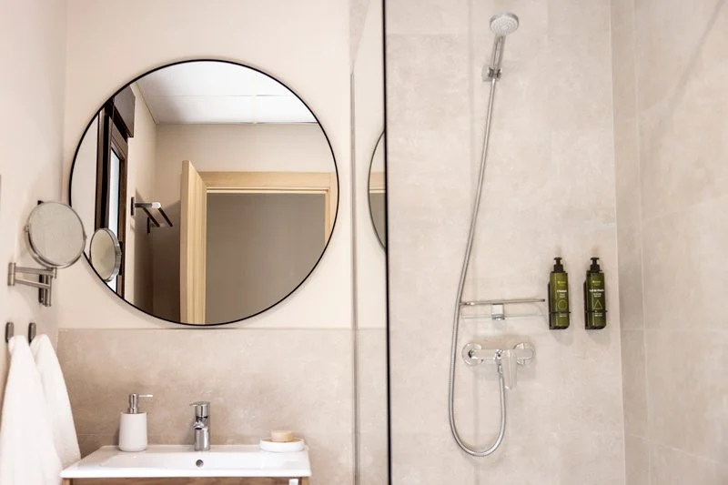 Ducha y lavabo en un baño moderno con espejos redondos y botellas de shampoo en la pared.